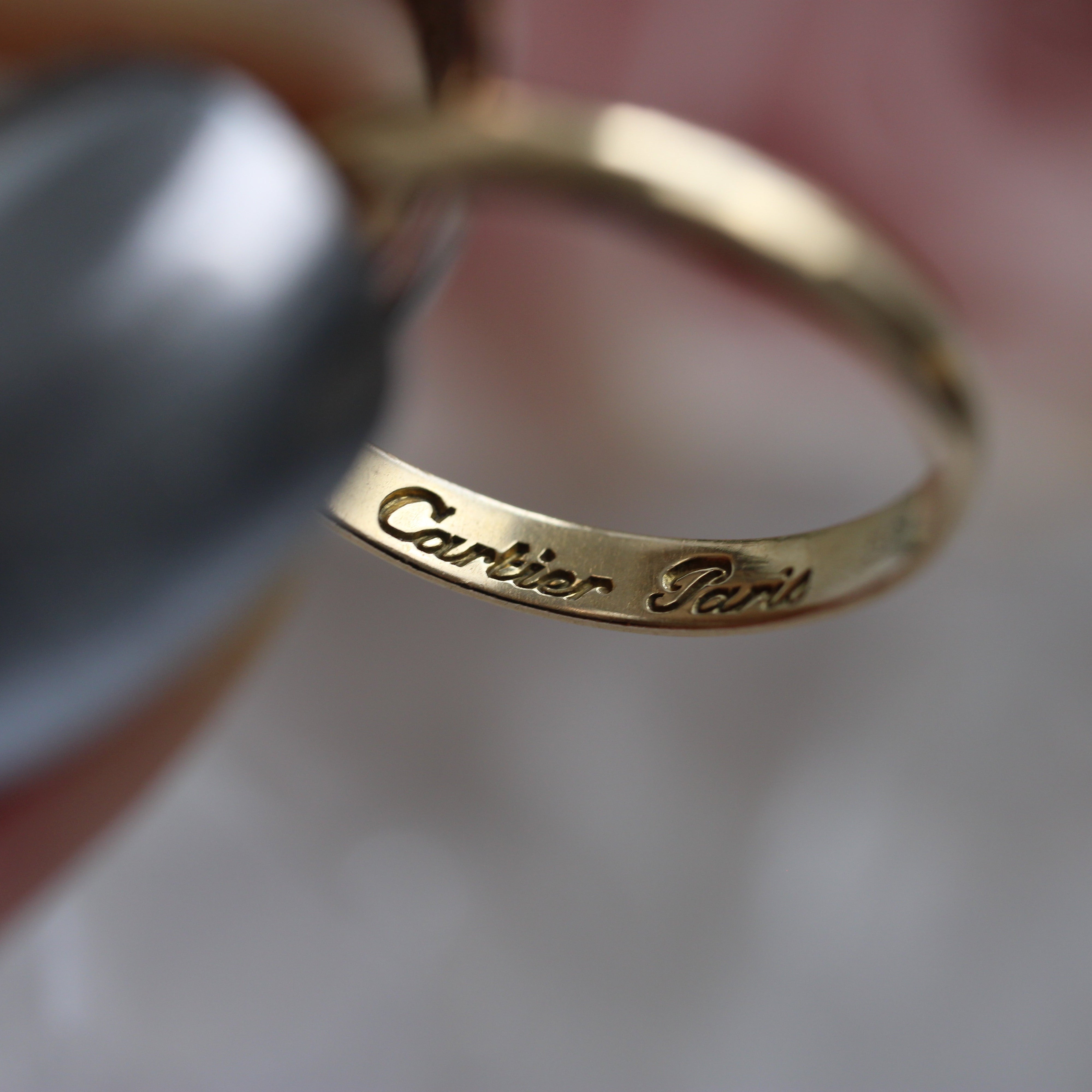 Gold Cartier ring held by a hand with a blurred background