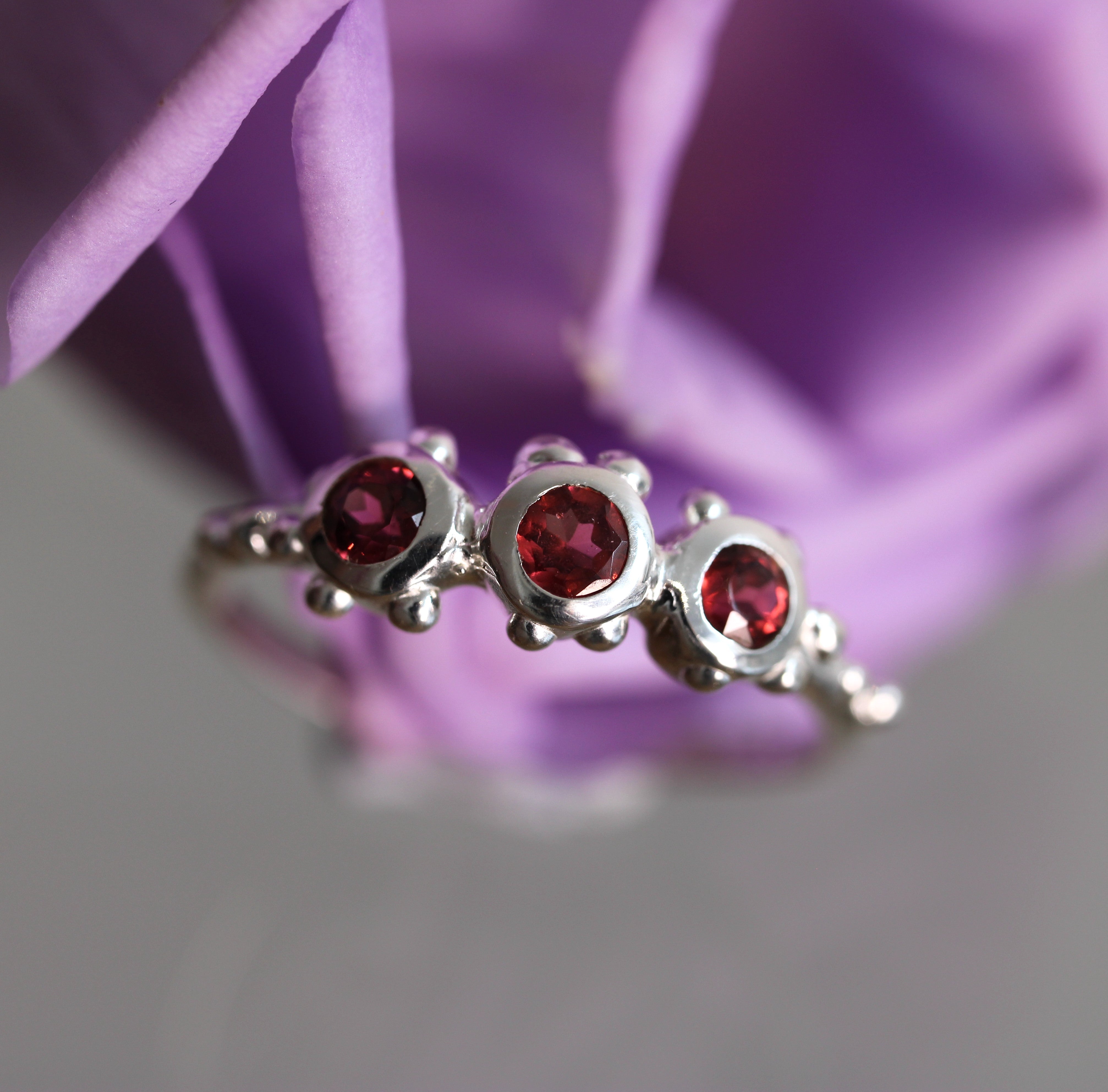 Silver ring with red gemstones against a purple flower background