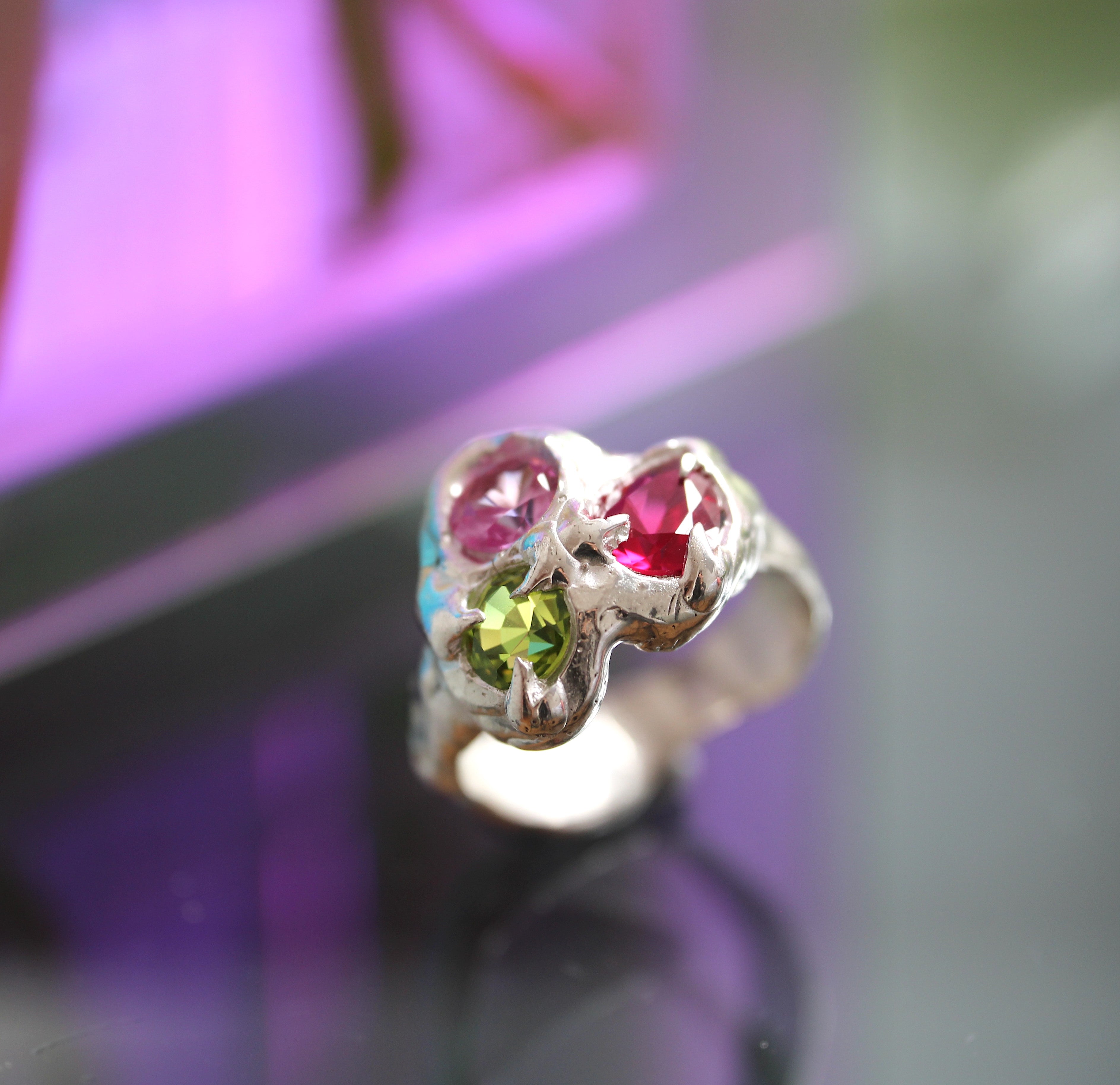 Silver ring with pink and green gemstones on a blurred background