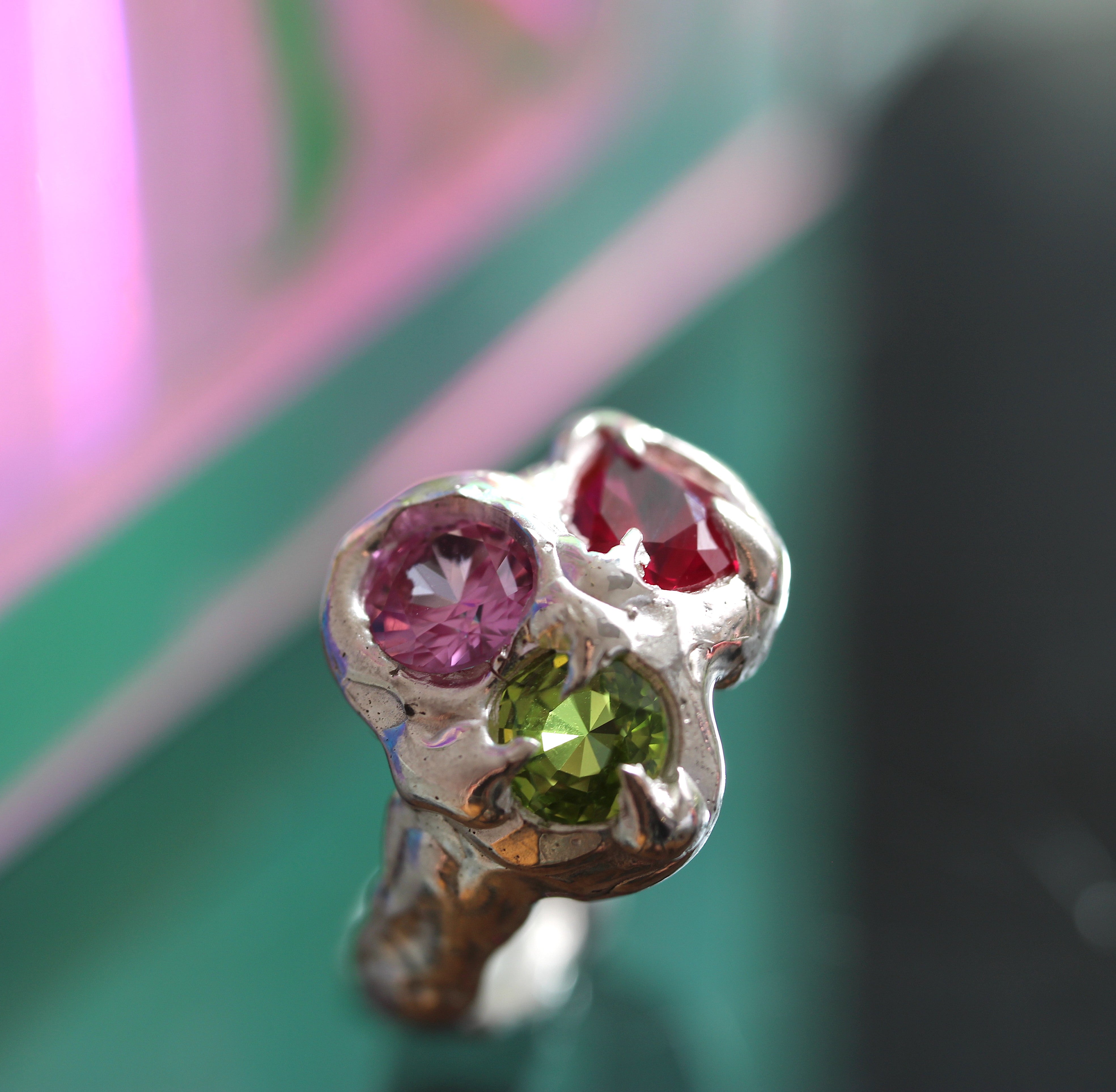 Silver ring with pink, red, and green gemstones on a blurred background