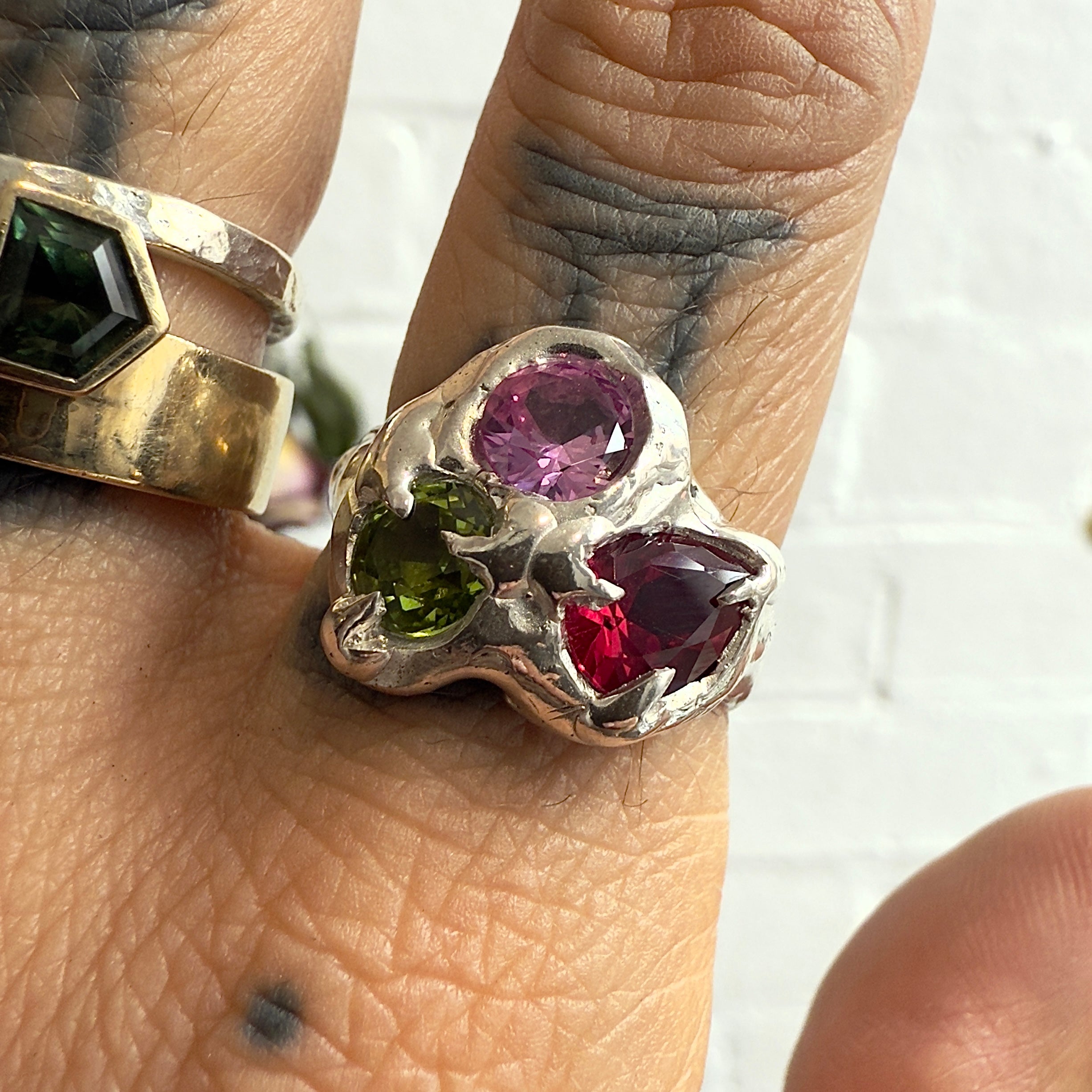 Close-up of a hand wearing a silver ring with colored gemstones on a white background