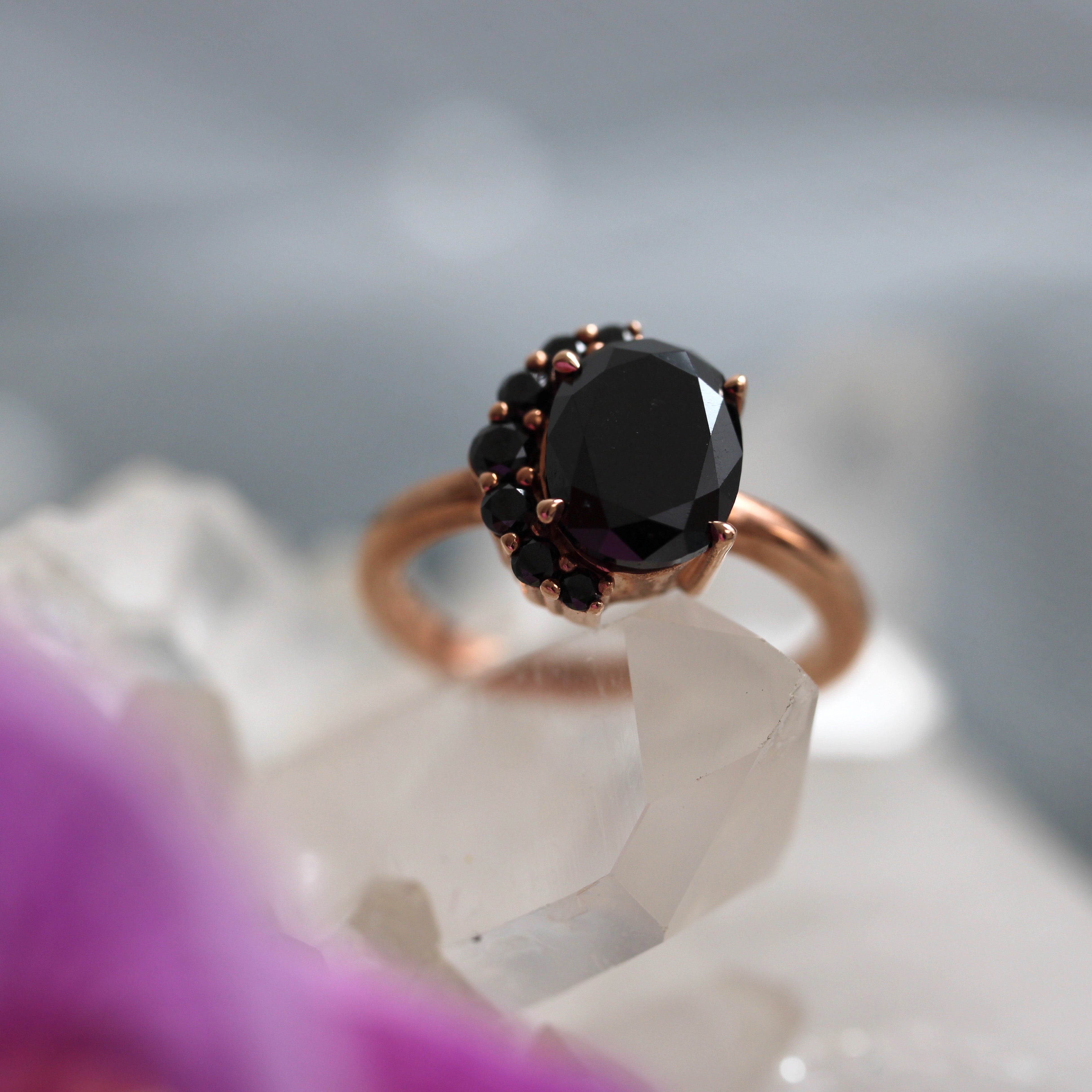 Rose gold ring with a large black diamond on a white stone surface