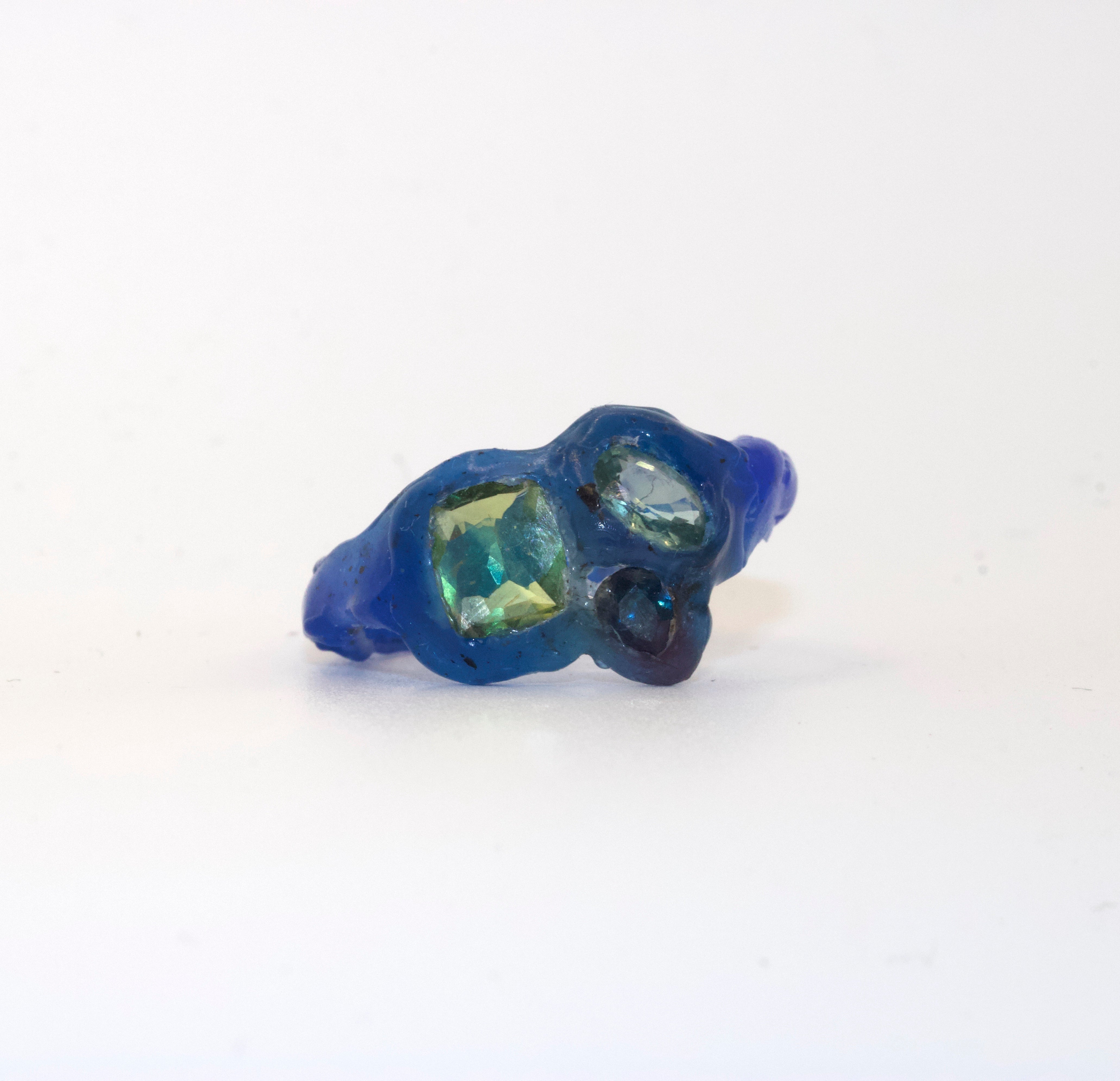Blue wax model ring with green gemstones on a white background