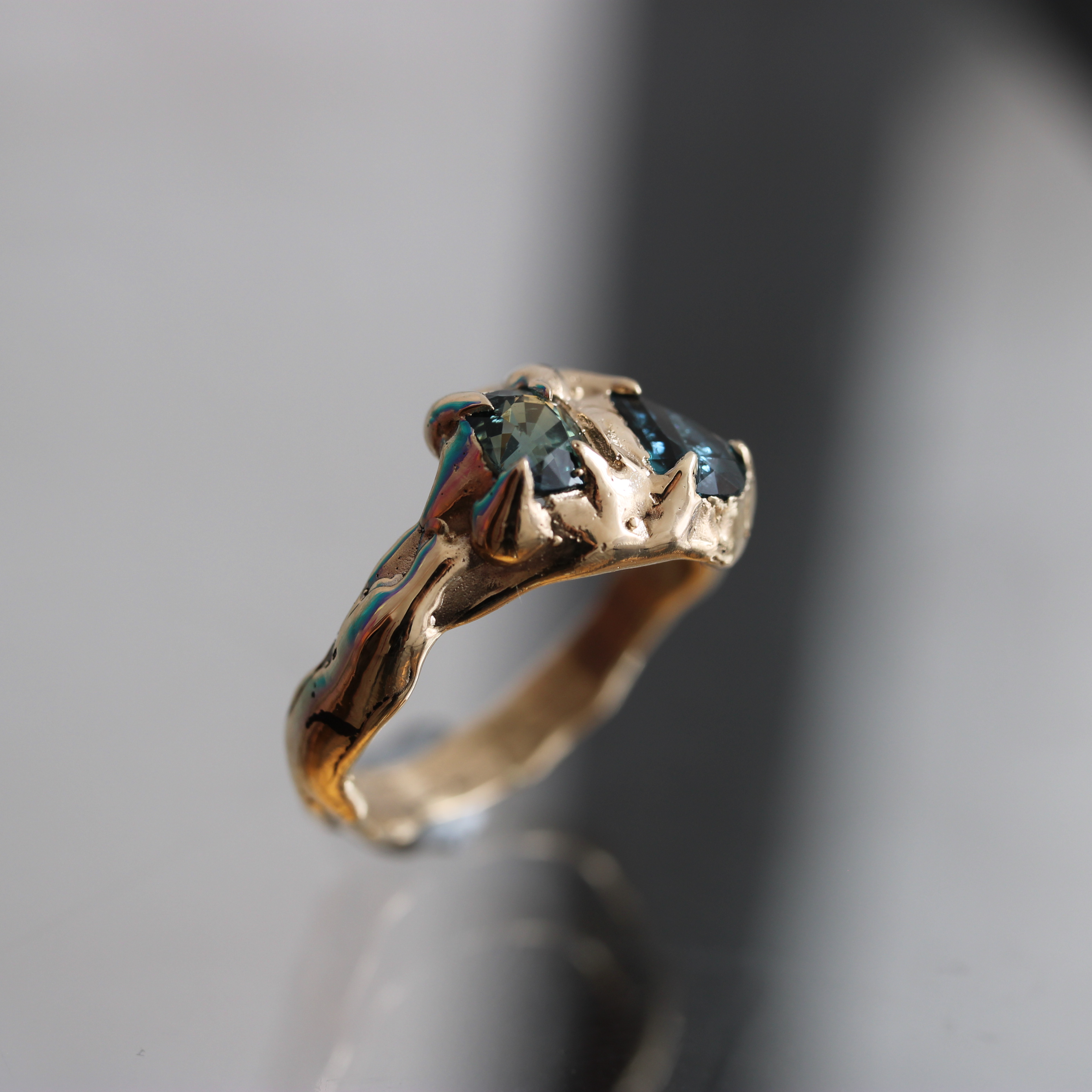 Gold ring with a central parttii sapphire gemstone on a gray background