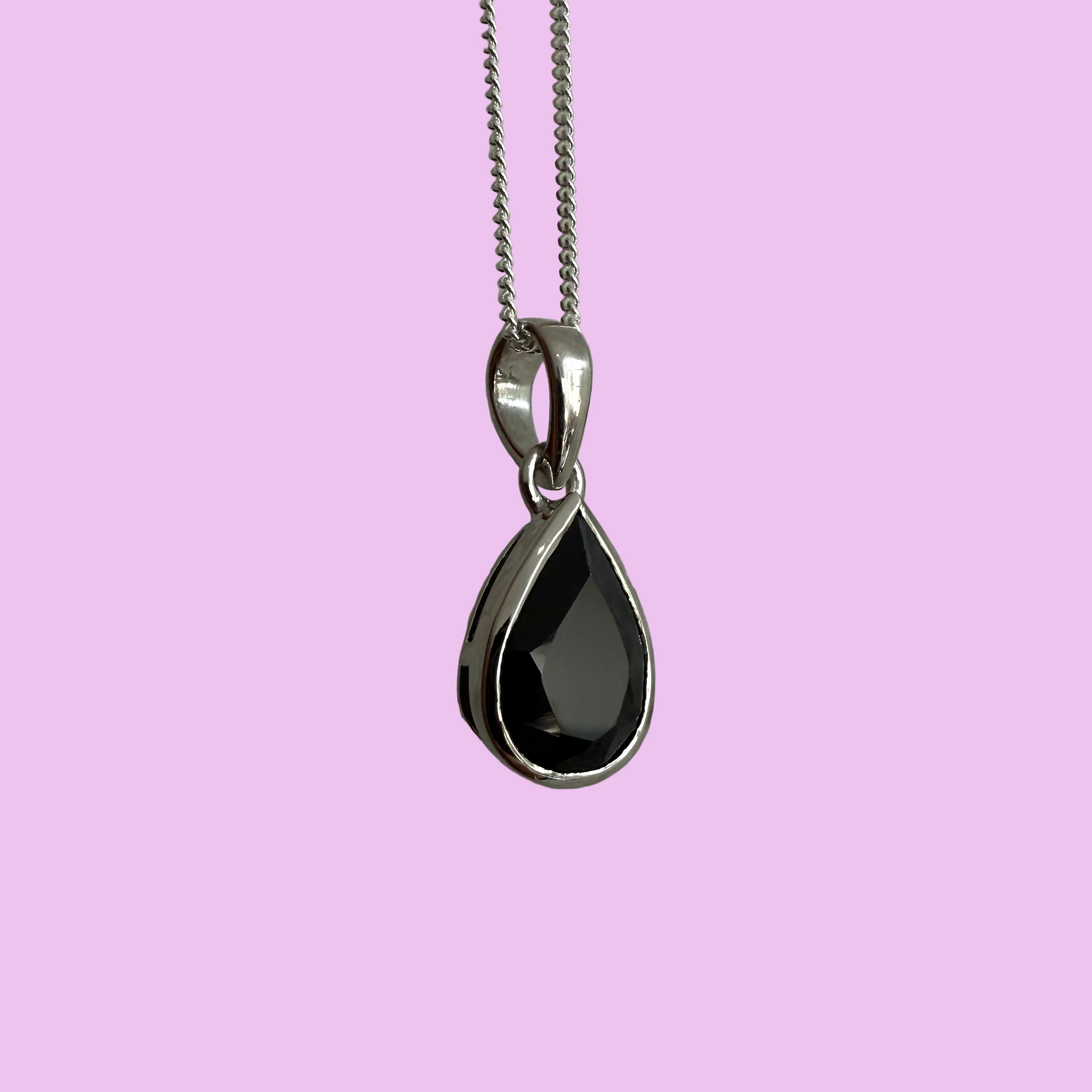 Teardrop-shaped black gemstone pendant on a silver chain against a gray background