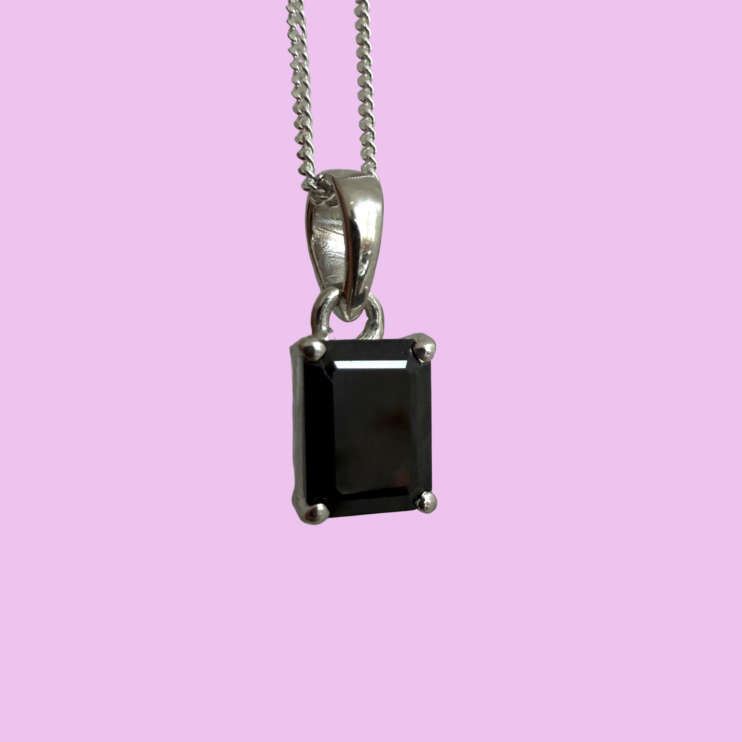 Silver pendant with a black gemstone on a chain against a textured gray background