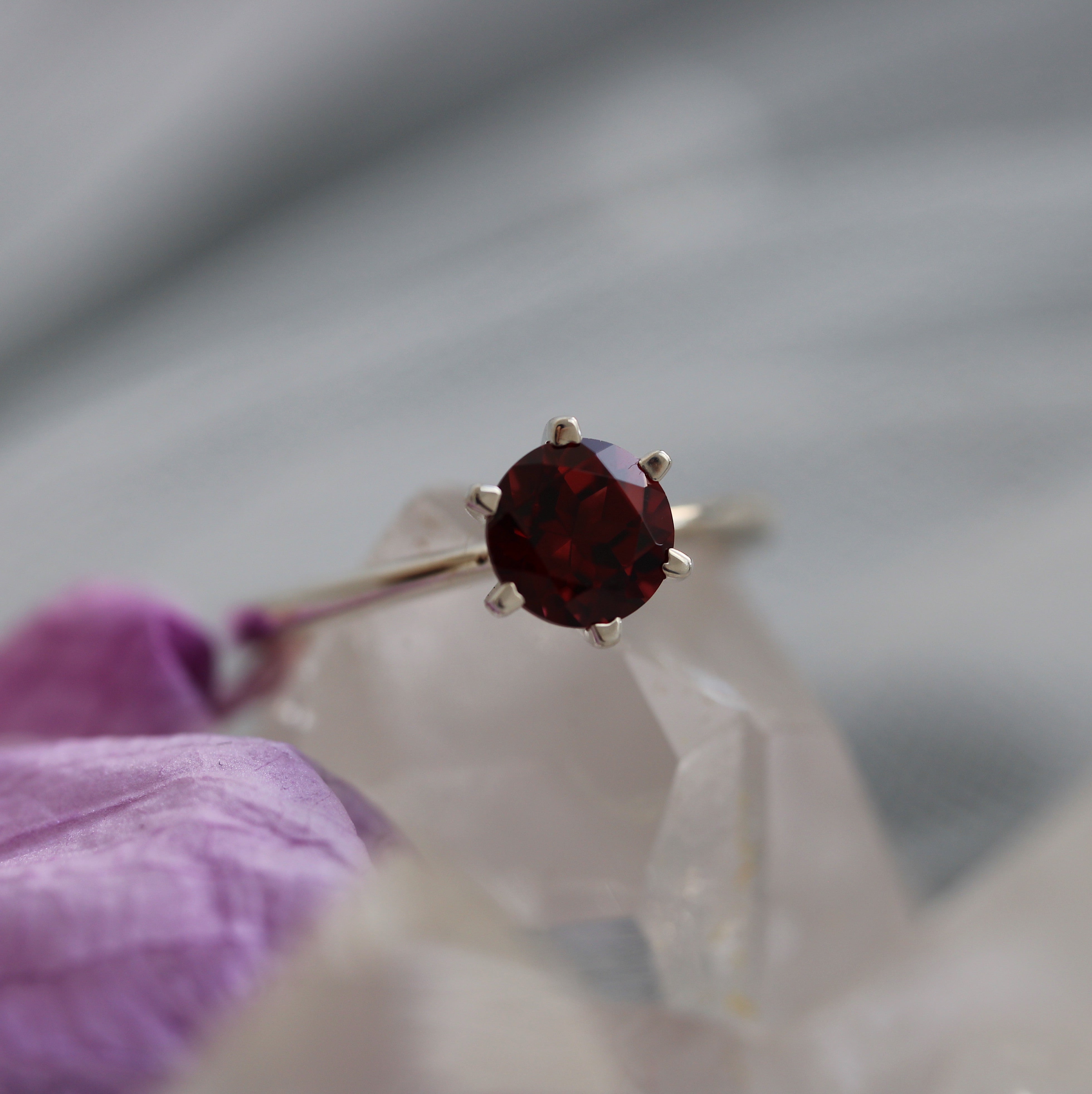 Gold ring with a red garnet gemstone held by a gloved hand against a gray background