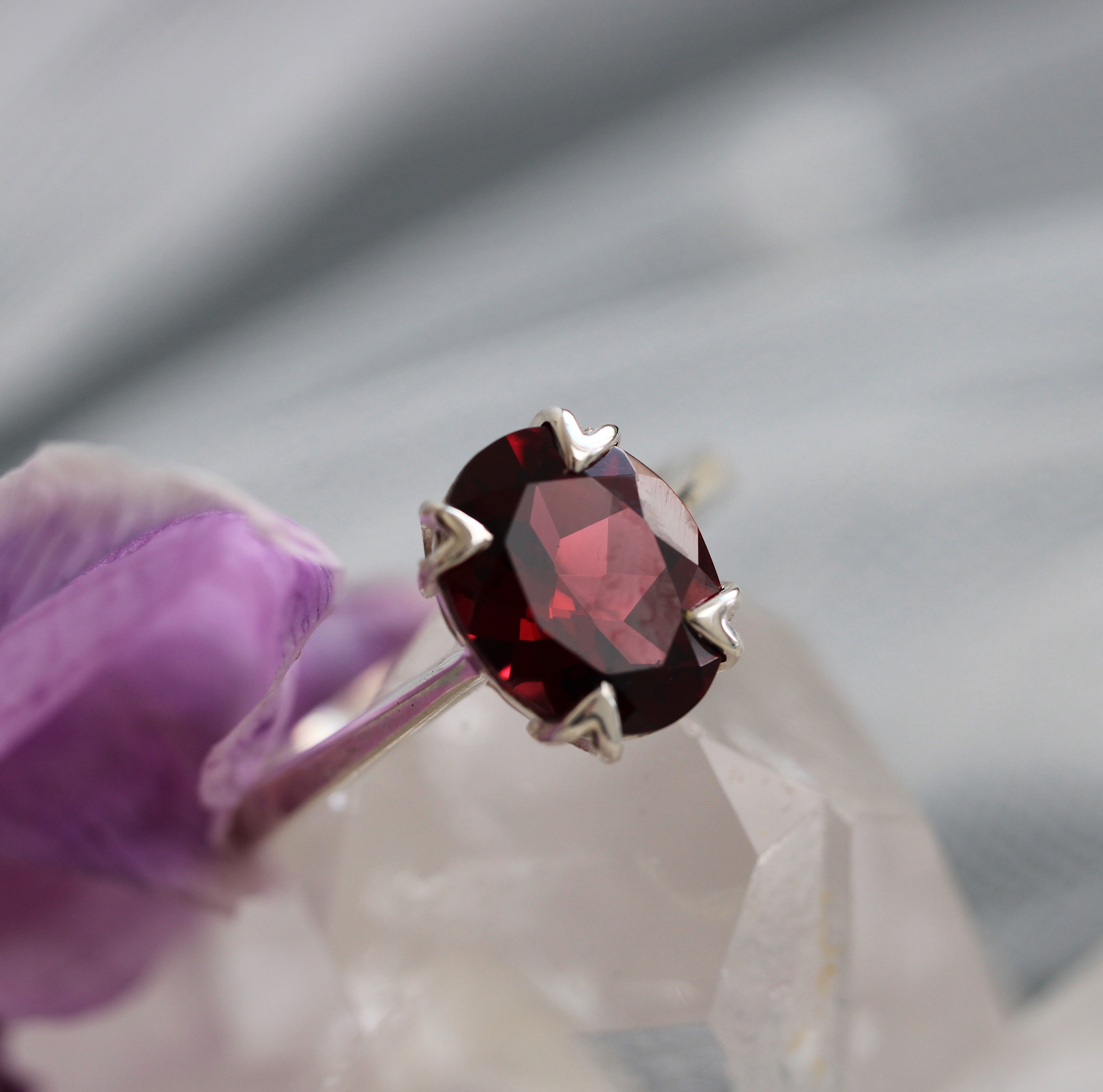 Ring with a red garnet gemstone held by a gloved hand against a neutral background
