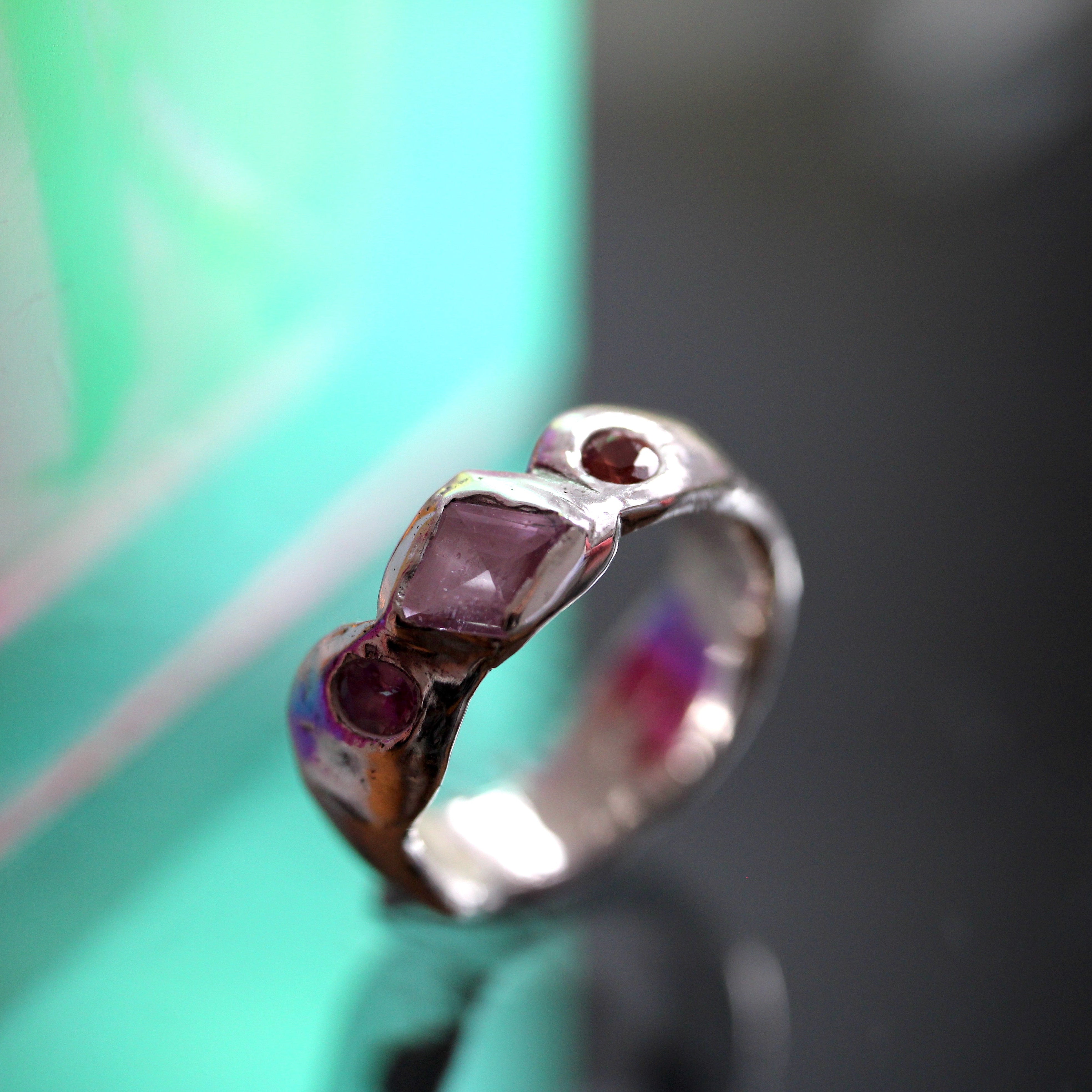 Silver ring with purple gemstones on a reflective surface with a blurred background