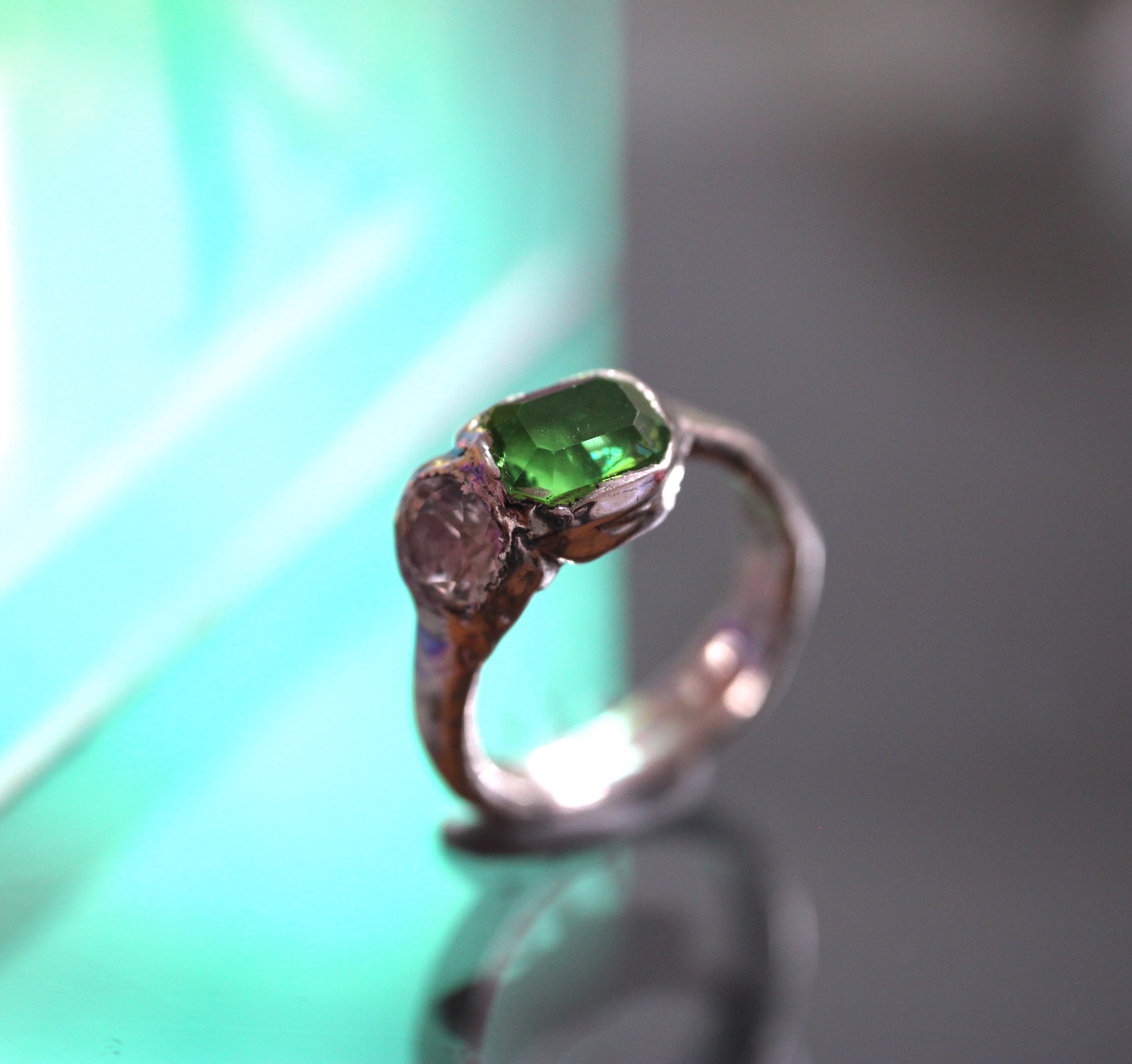 Silver ring with a green gemstone on a reflective surface by windfall jewellery