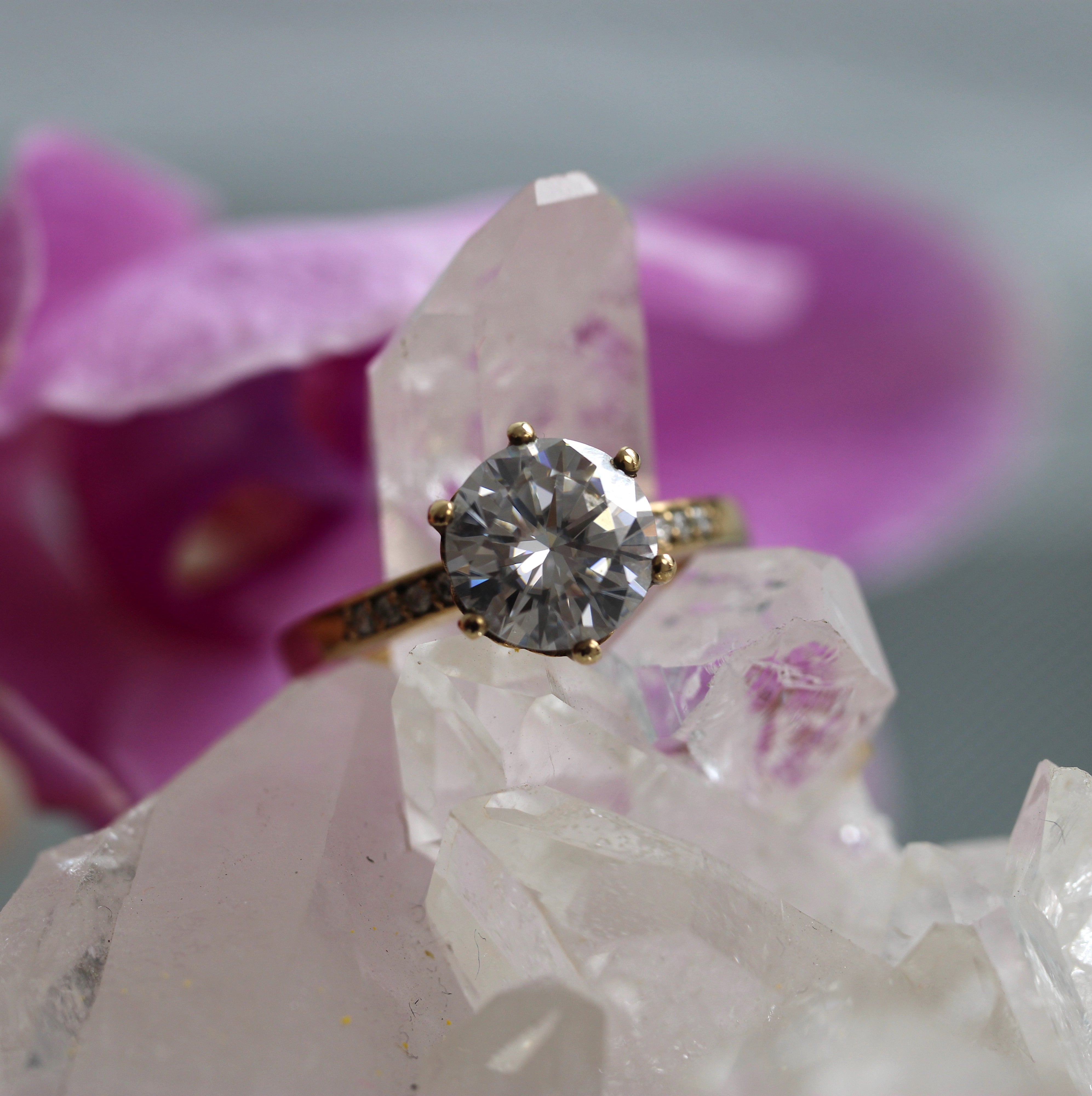 Gold ring with a diamond on a crystal with pink flowers in the background