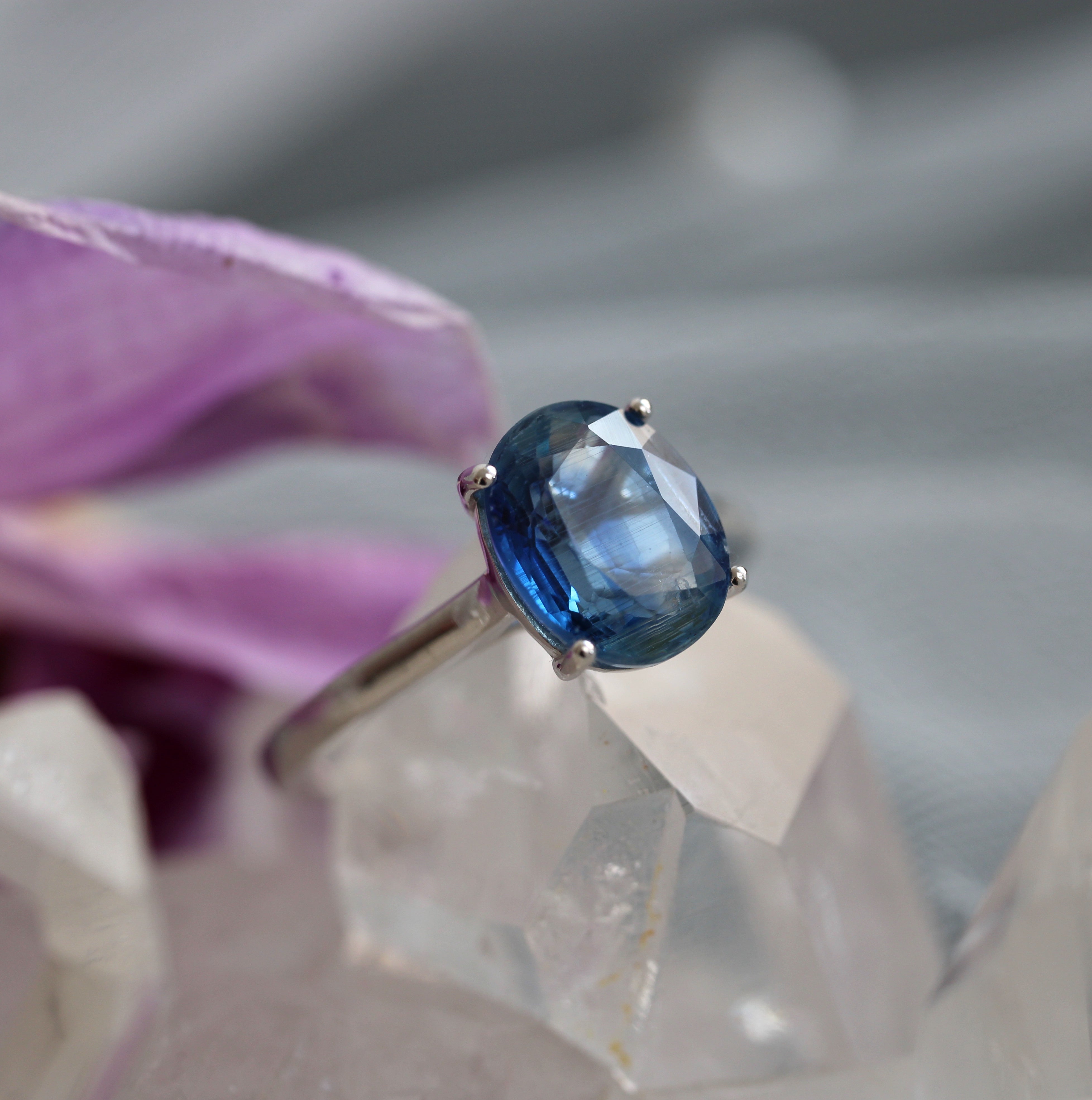 Ring with a blue kyanite gemstone held against a blurred natural background