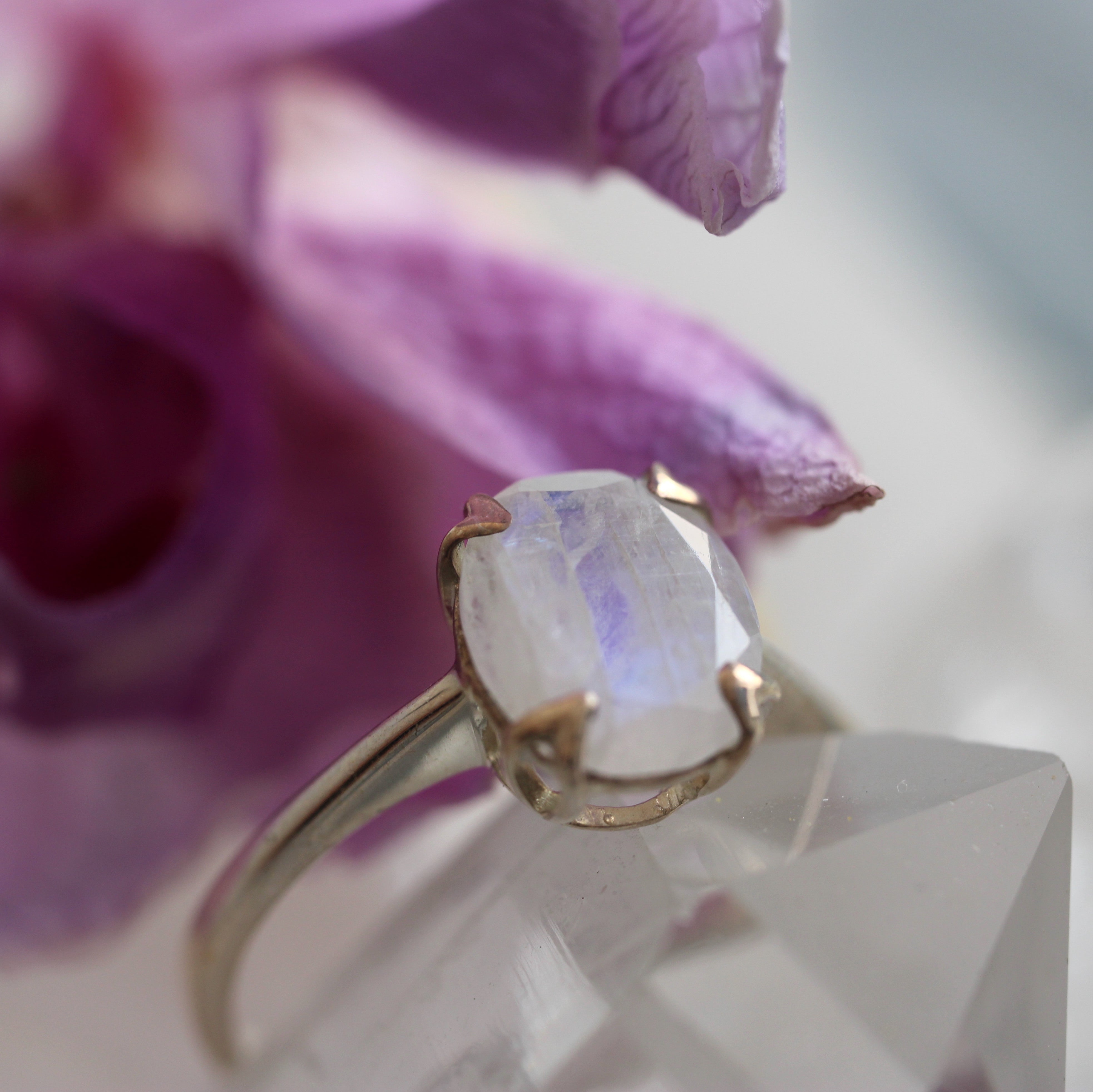 Gold ring with a moonstone on a crystal surface with a blurred purple flower in the background