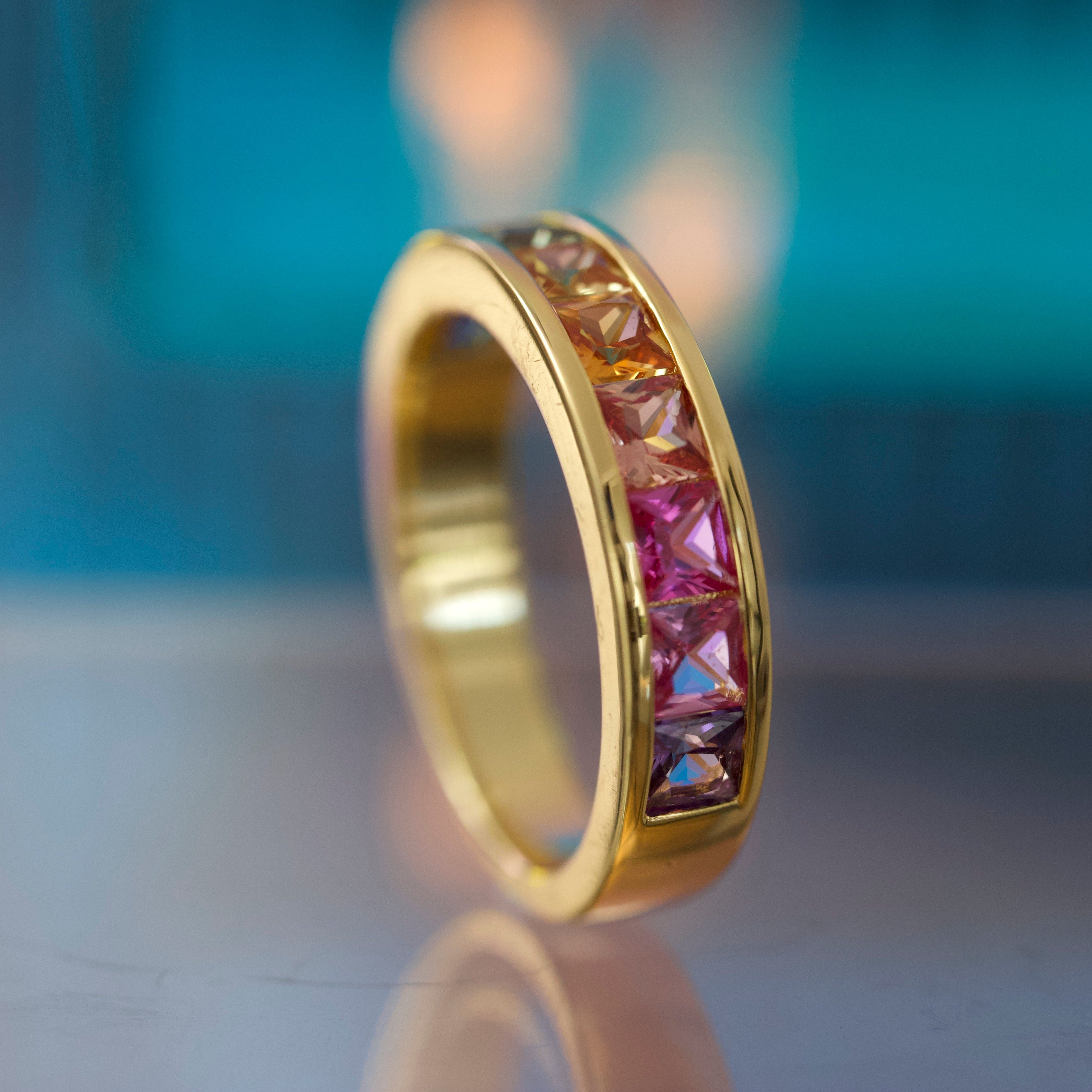Gold ring with rainbow gemstones on a reflective surface with a blurred background