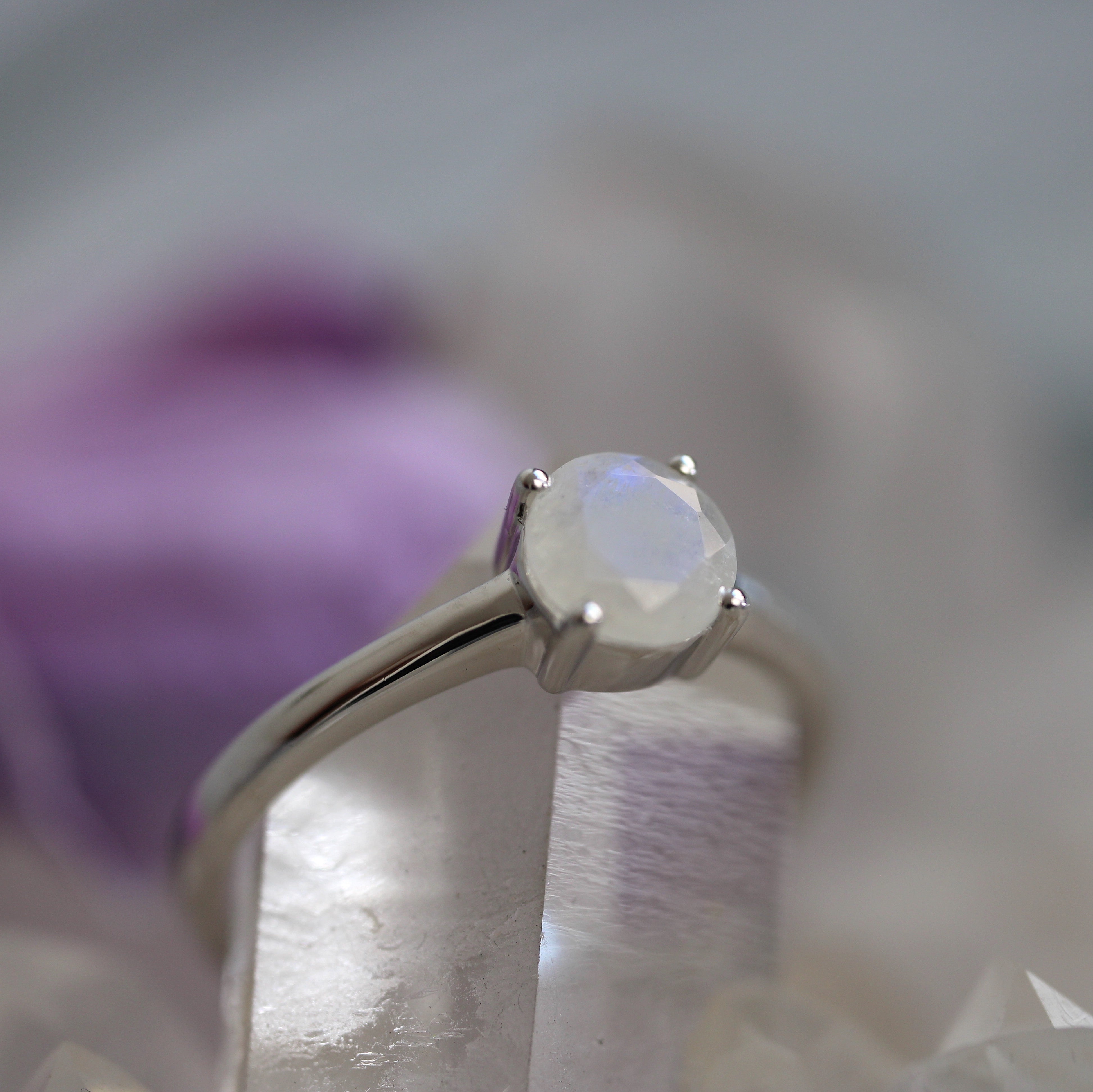 Silver ring with a round rainbow moonstone gemstone on a blurred background