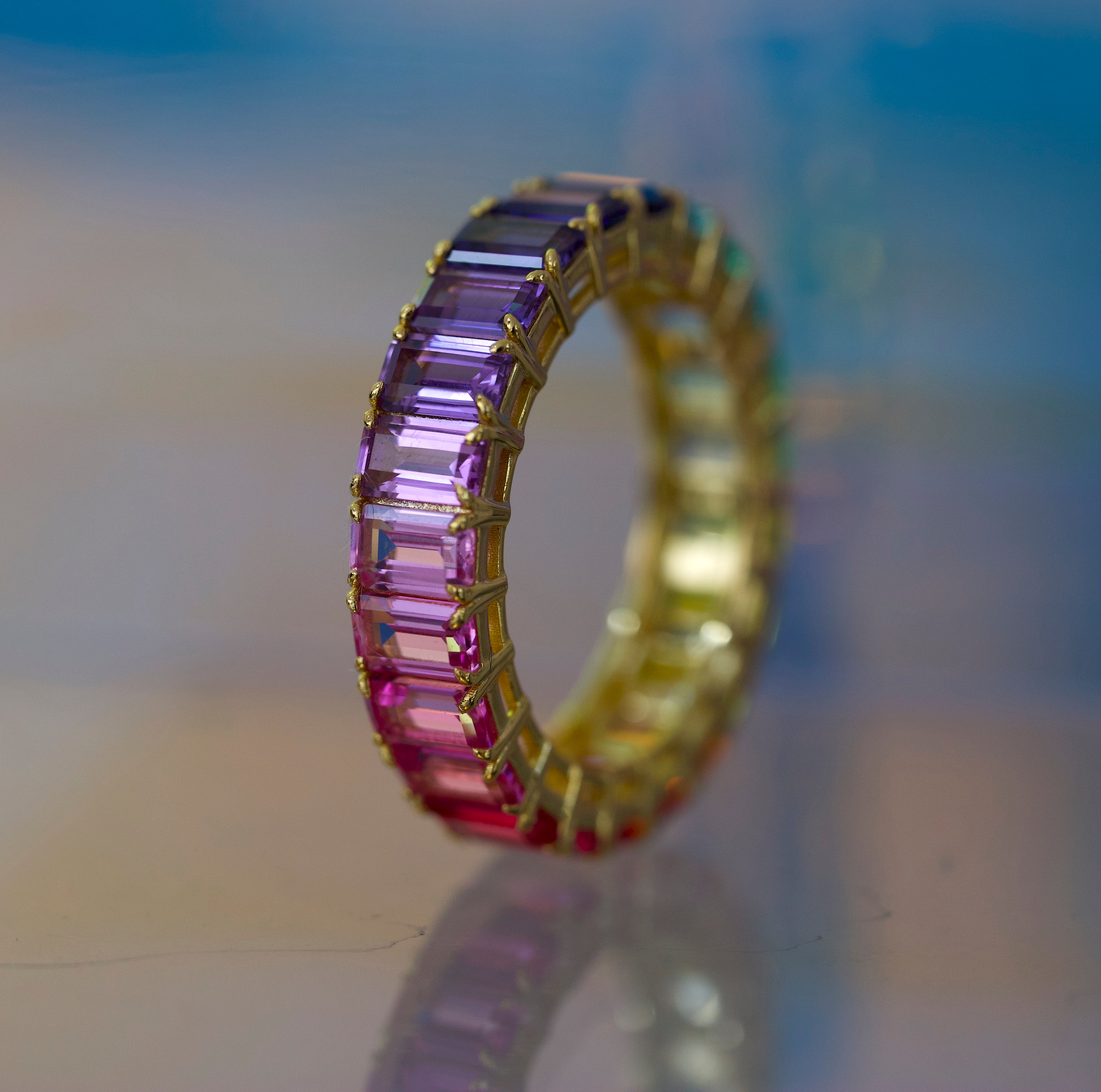 Gold ring with purple gemstones on a reflective surface