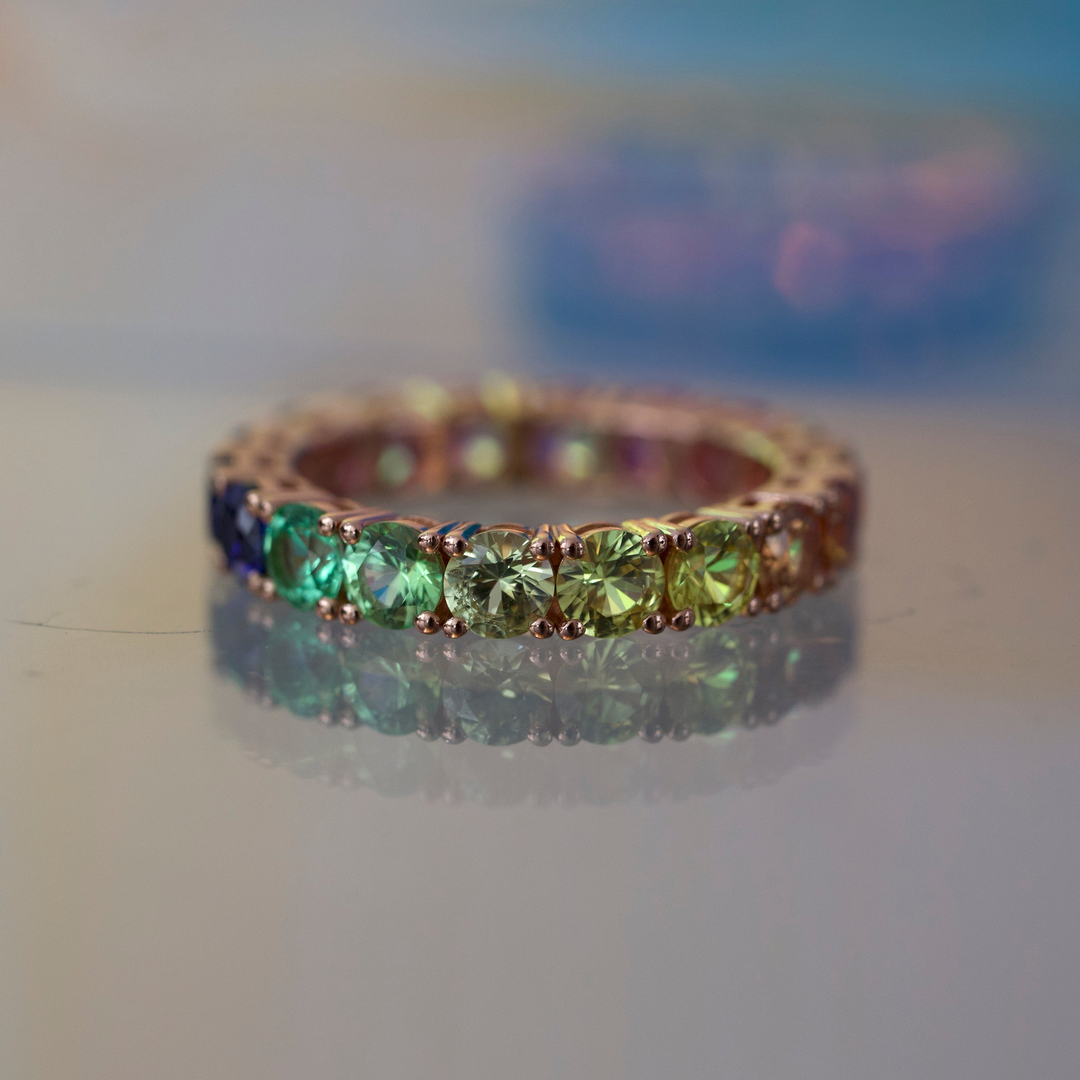 Gold ring with green gemstones on a reflective surface
