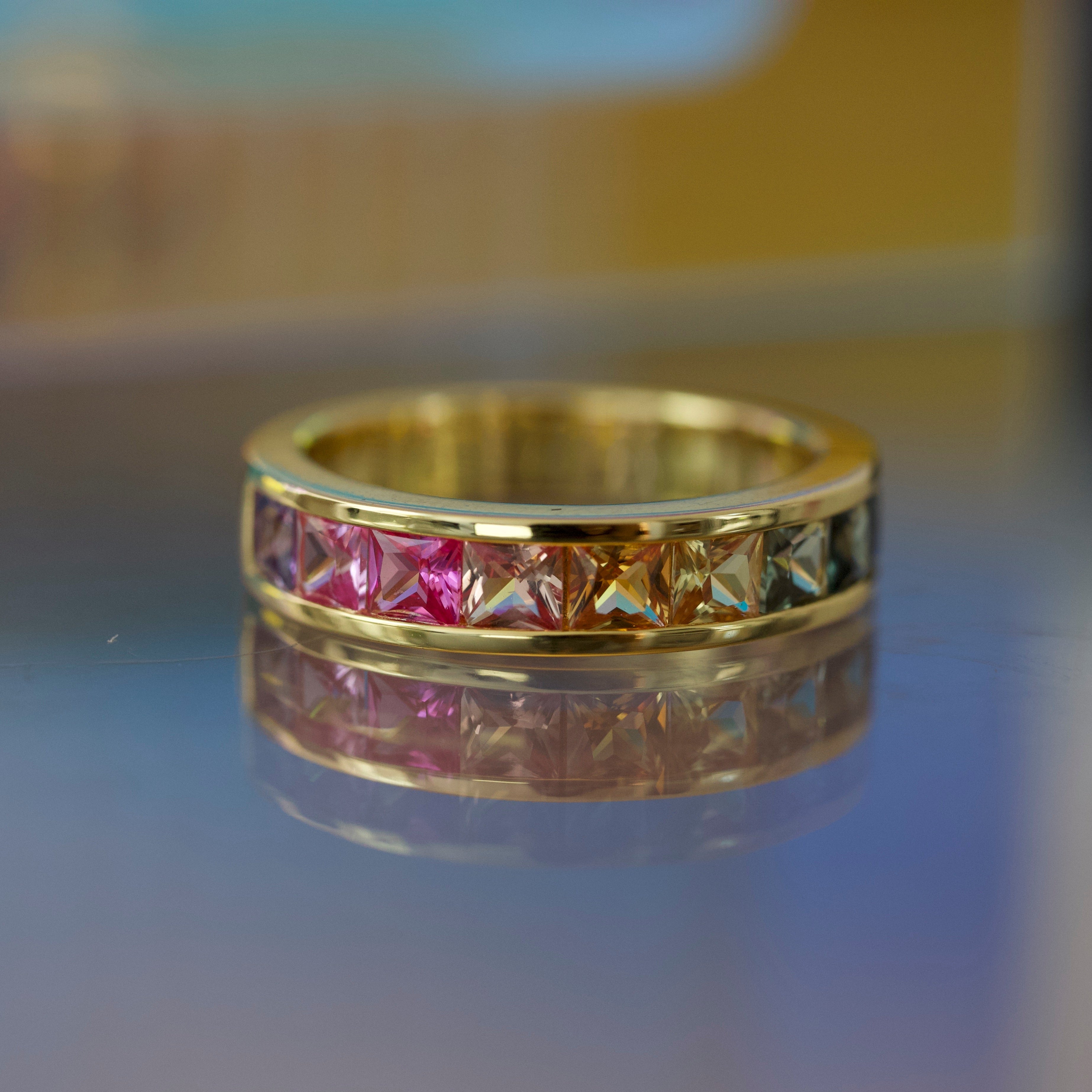 Gold ring with rainbow multicolored gemstones on a reflective surface