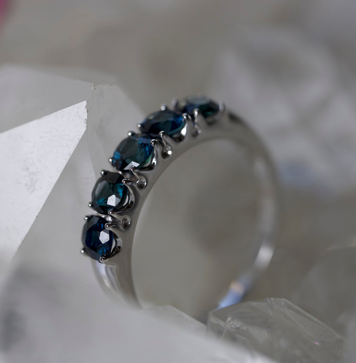 A silver-toned ring featuring a row of oval dark blue gemstones, resting on a textured white crystal surface.