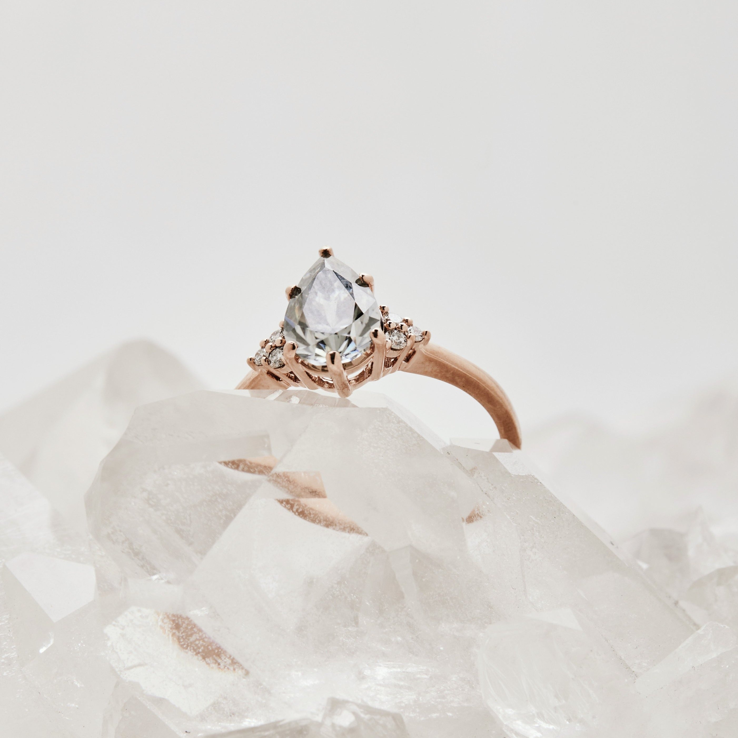 Close-up of a unique salt and pepper pear diamond ring photographed on clear quartz