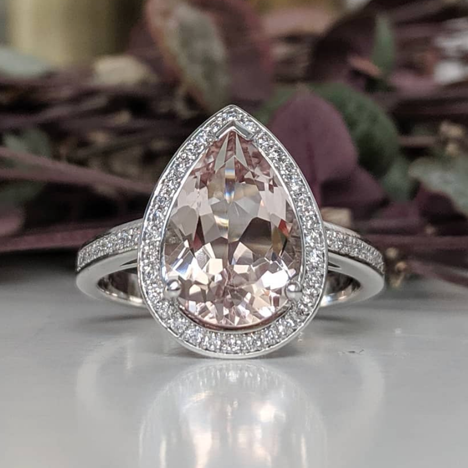 Morganite Pear halo diamond engagement ring paired with matching wedding band shown on flower background — classic bridal set in white gold