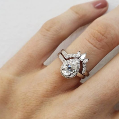 Pear halo diamond engagement ring paired with matching wedding band shown on hand — classic bridal set in white gold
