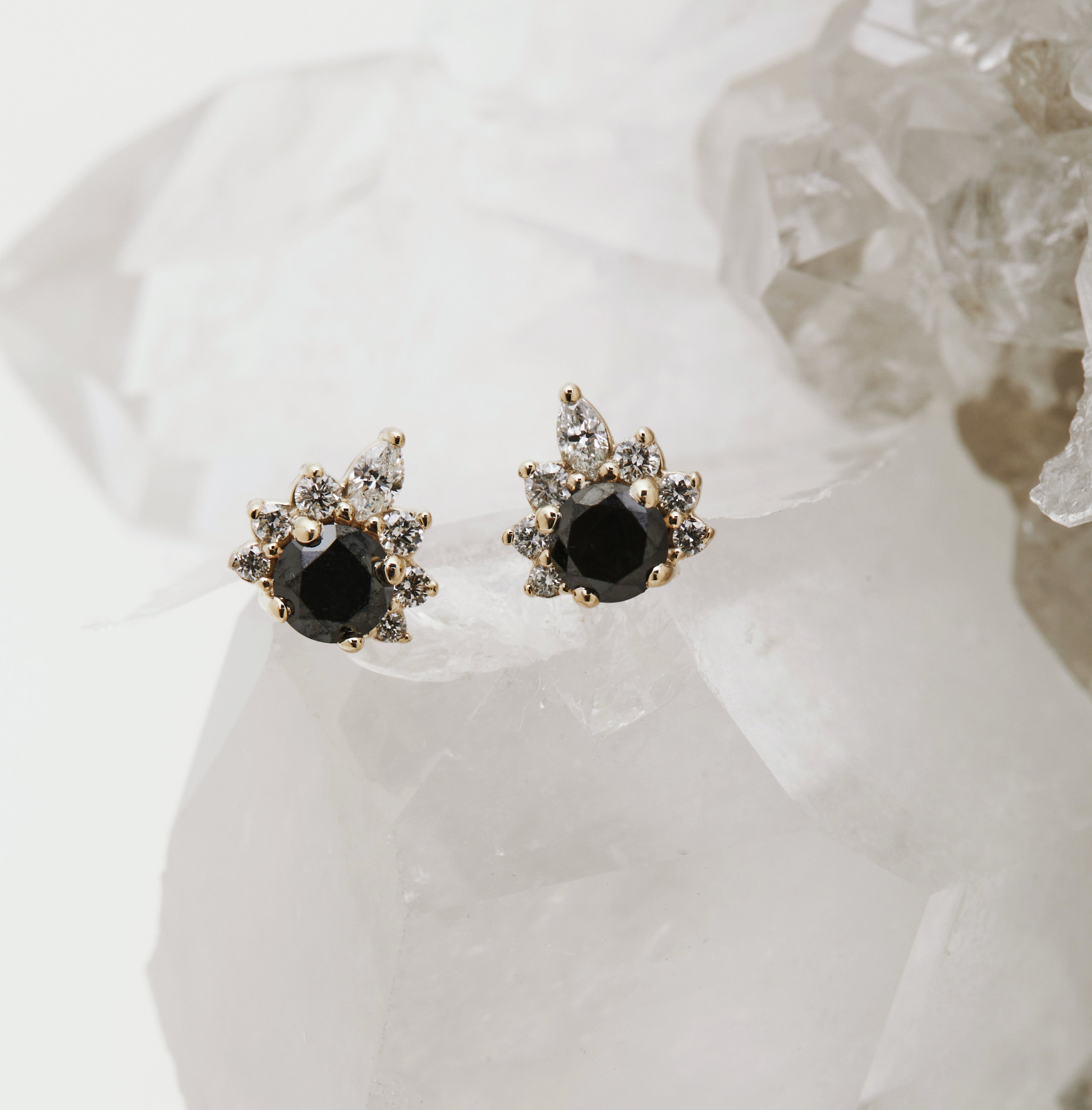 A pair of earrings with a central diamond and smaller accent diamonds set in a gold-colored frame, displayed on a crystal.
