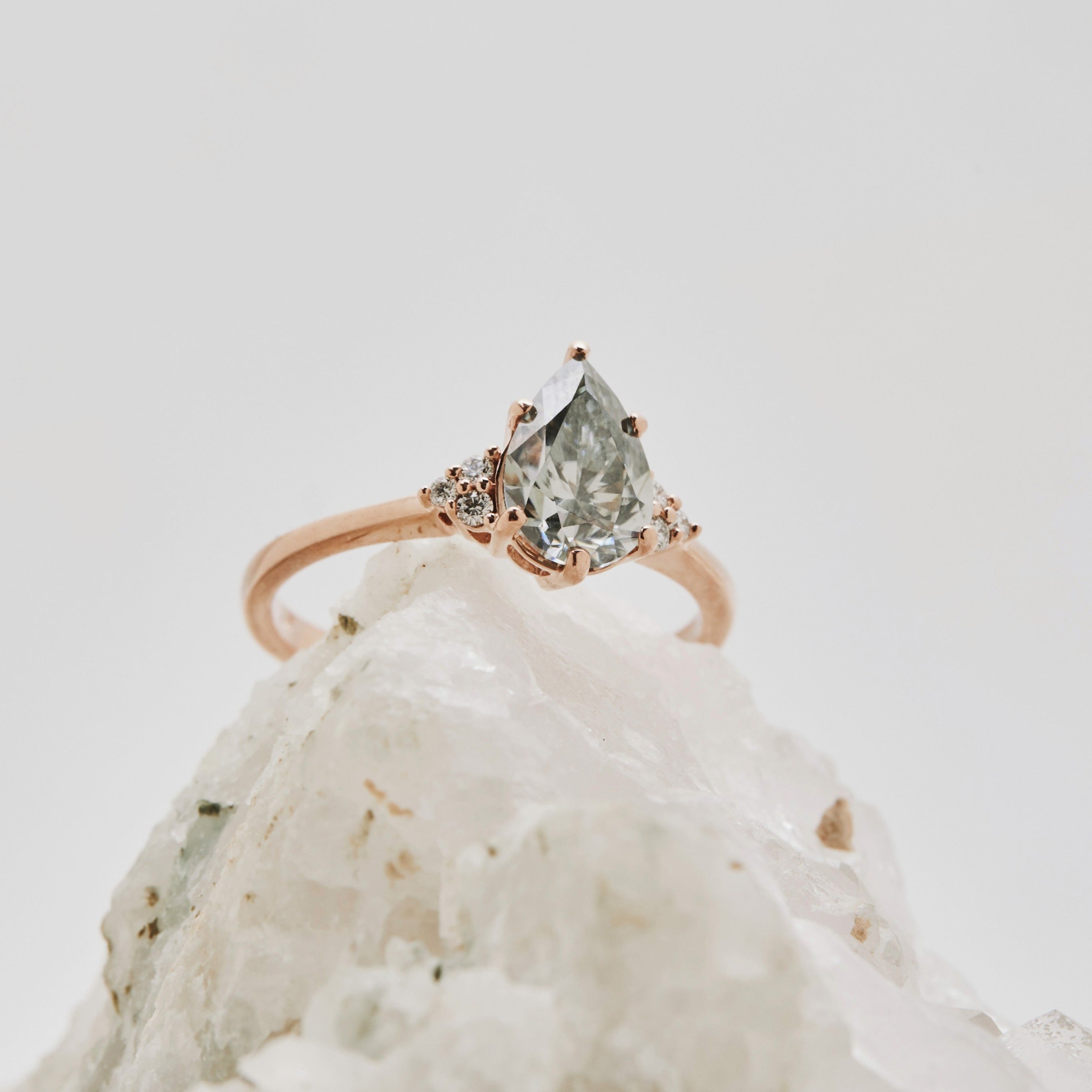 Close-up of a unique salt and pepper pear diamond ring photographed on clear quartz