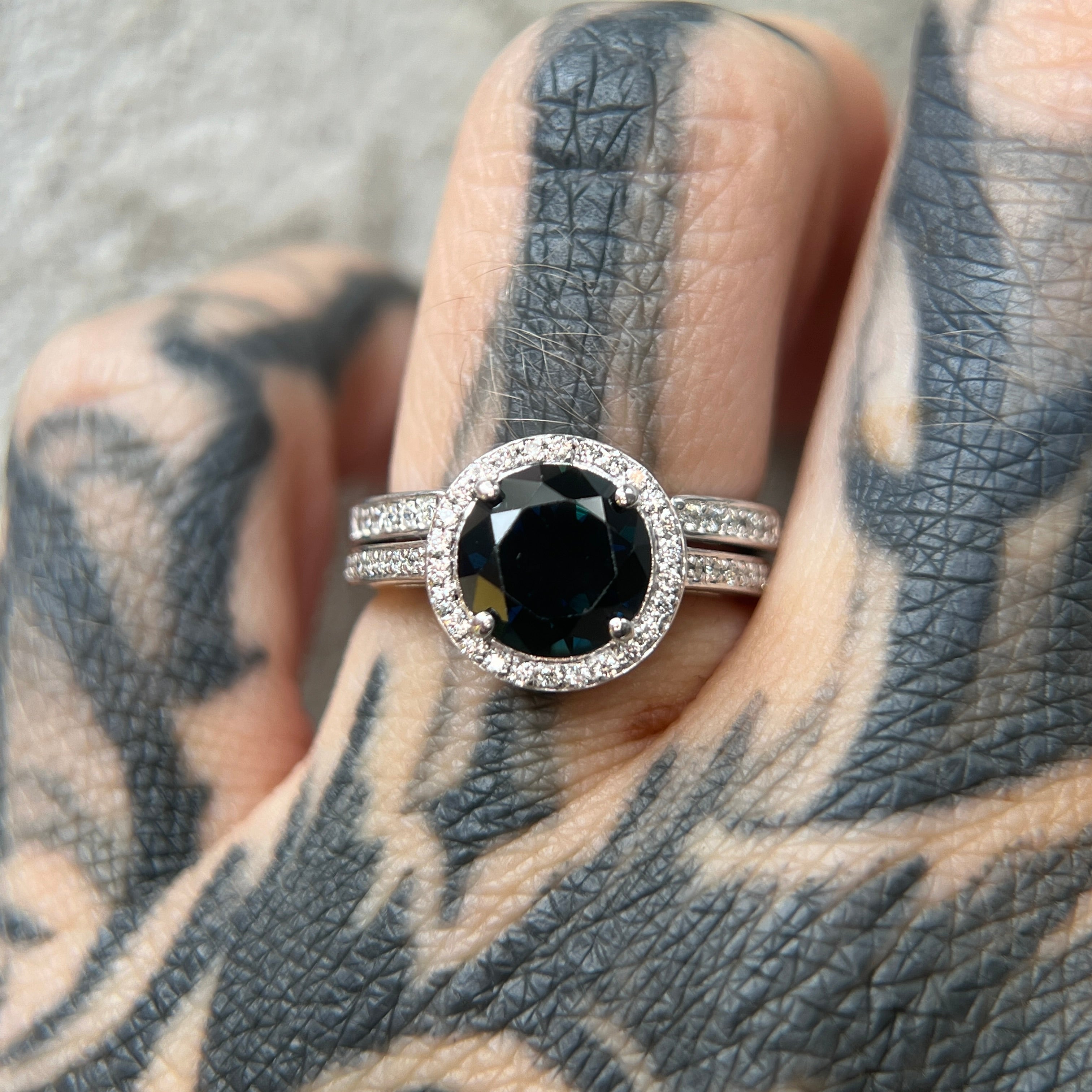 Round halo diamond engagement ring in yellow gold with a thicker pavé band, photographed on a tattooed hand — elegant bridal jewelry