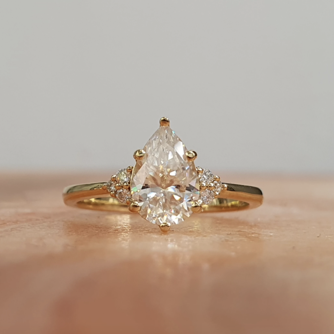A pear-shaped diamond ring with three white diamond accents on the sides, set in a rose gold band.
