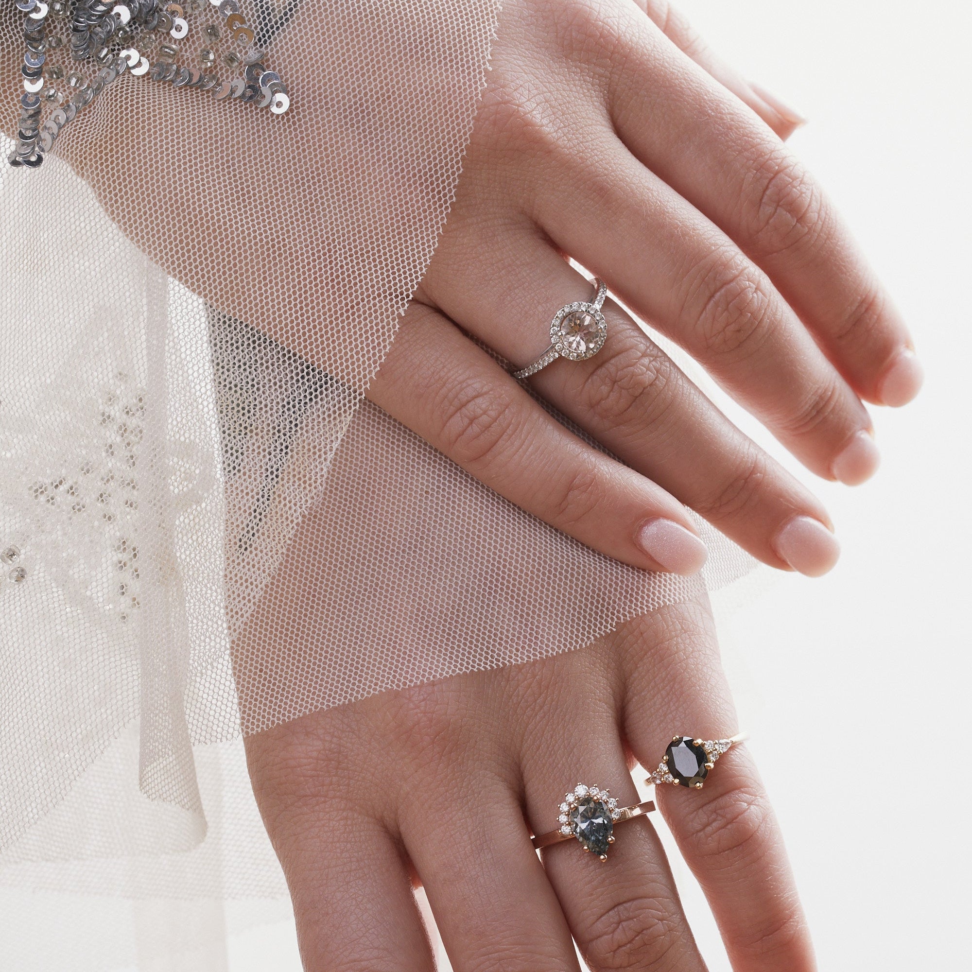 Close-up of hands wearing two rings with gemstones on a light background