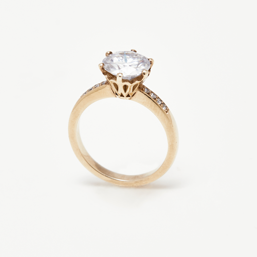 Poppy Solitaire diamond engagement ring in yellow gold with six-prong setting and pavé band, angled side view on white background.