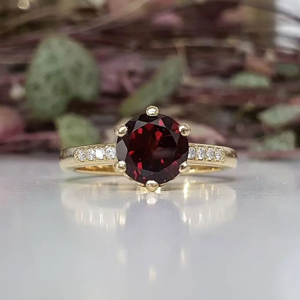 Poppy Solitaire garnetengagement ring in yellow gold with six-prong setting and pavé band, angled side view on white background.