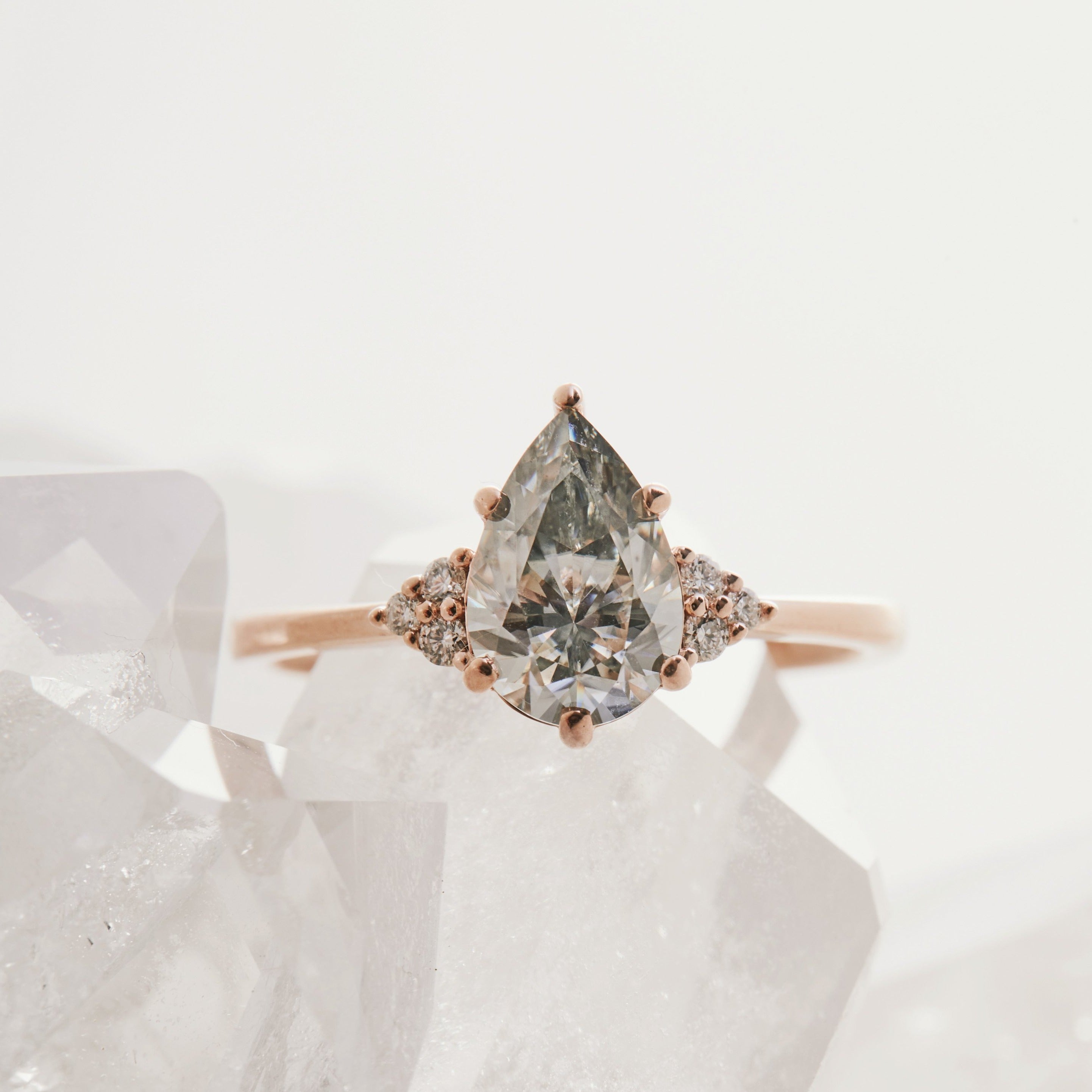 A pear-shaped diamond ring with three white diamond accents on the sides, set in a rose gold band.