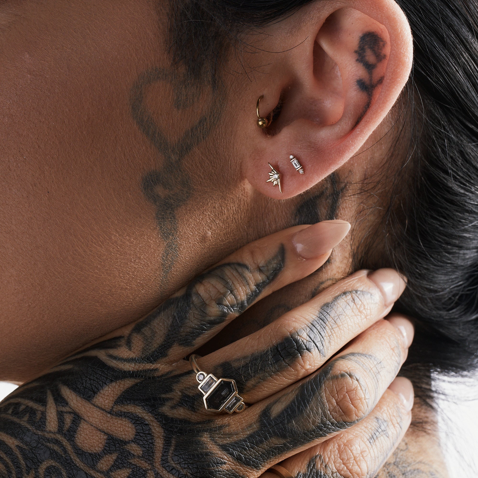 Close-up of a person with tattoos on their neck, ear, and hands wearing rings.