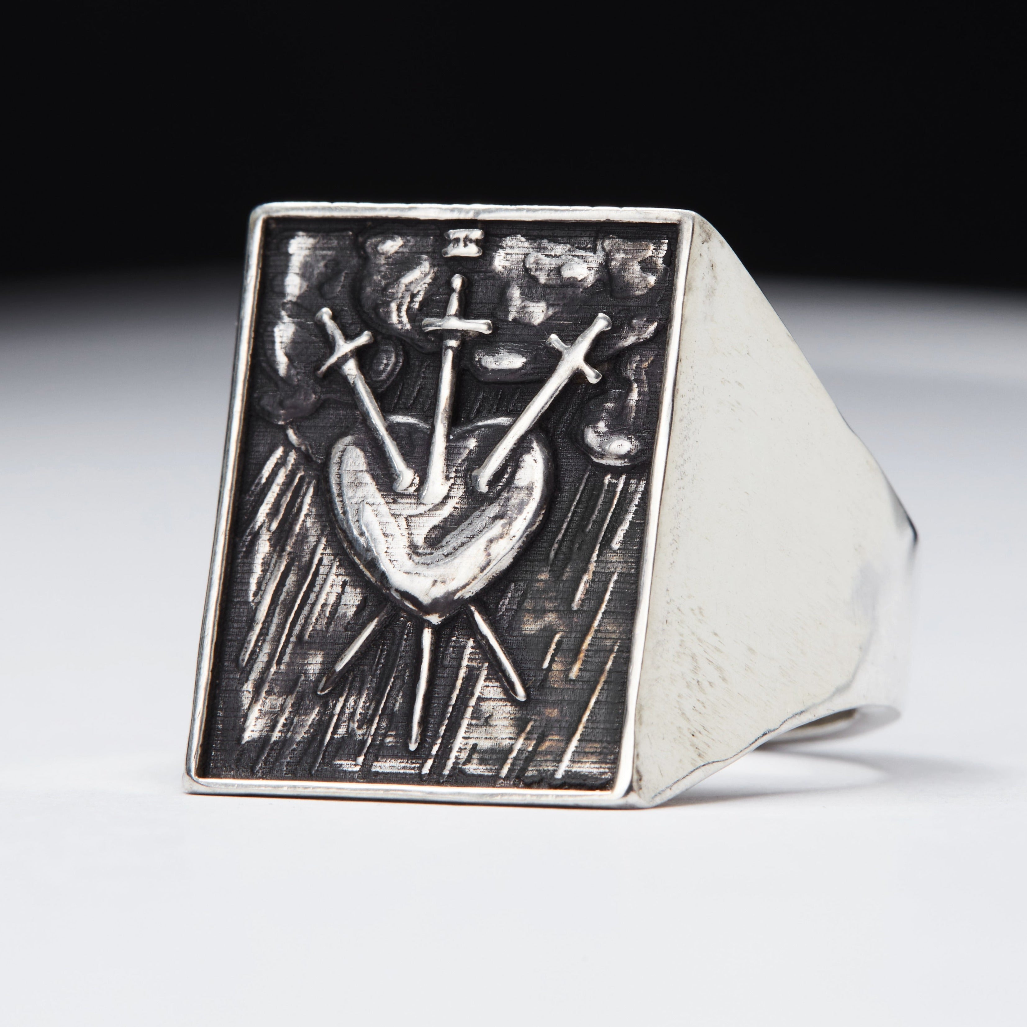 A signet ring with a design that includes a sword and a heart, likely representing the tarot card 'Three of Swords'.
