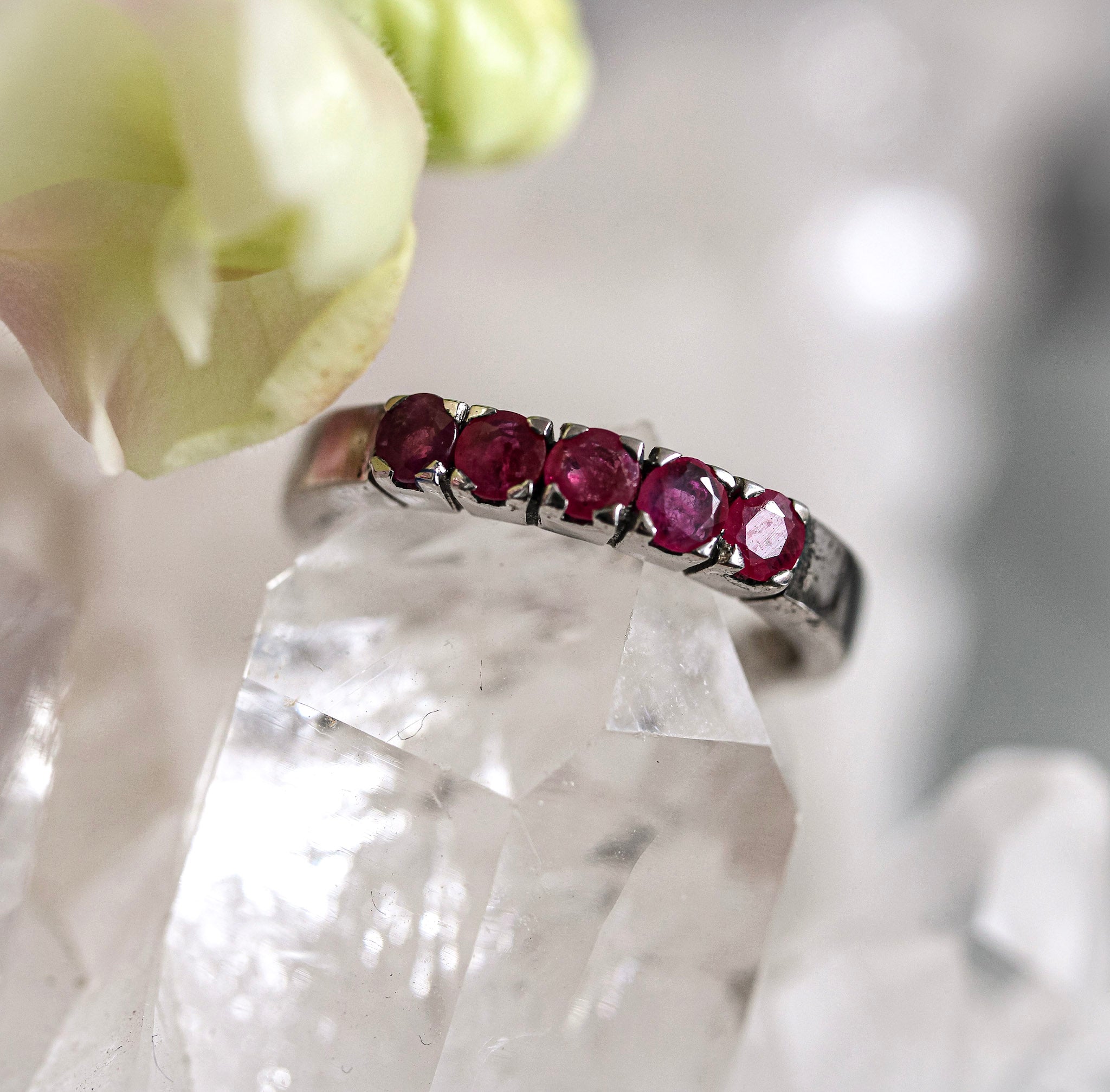 Silver ring with red ruby gemstones on a crystal surface with a blurred flower in the background
