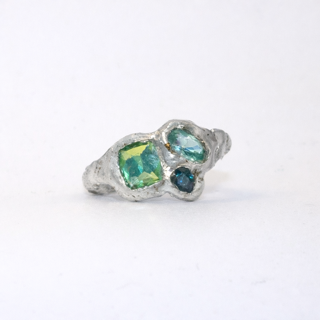 Silver ring with green and blue gemstones on a white background