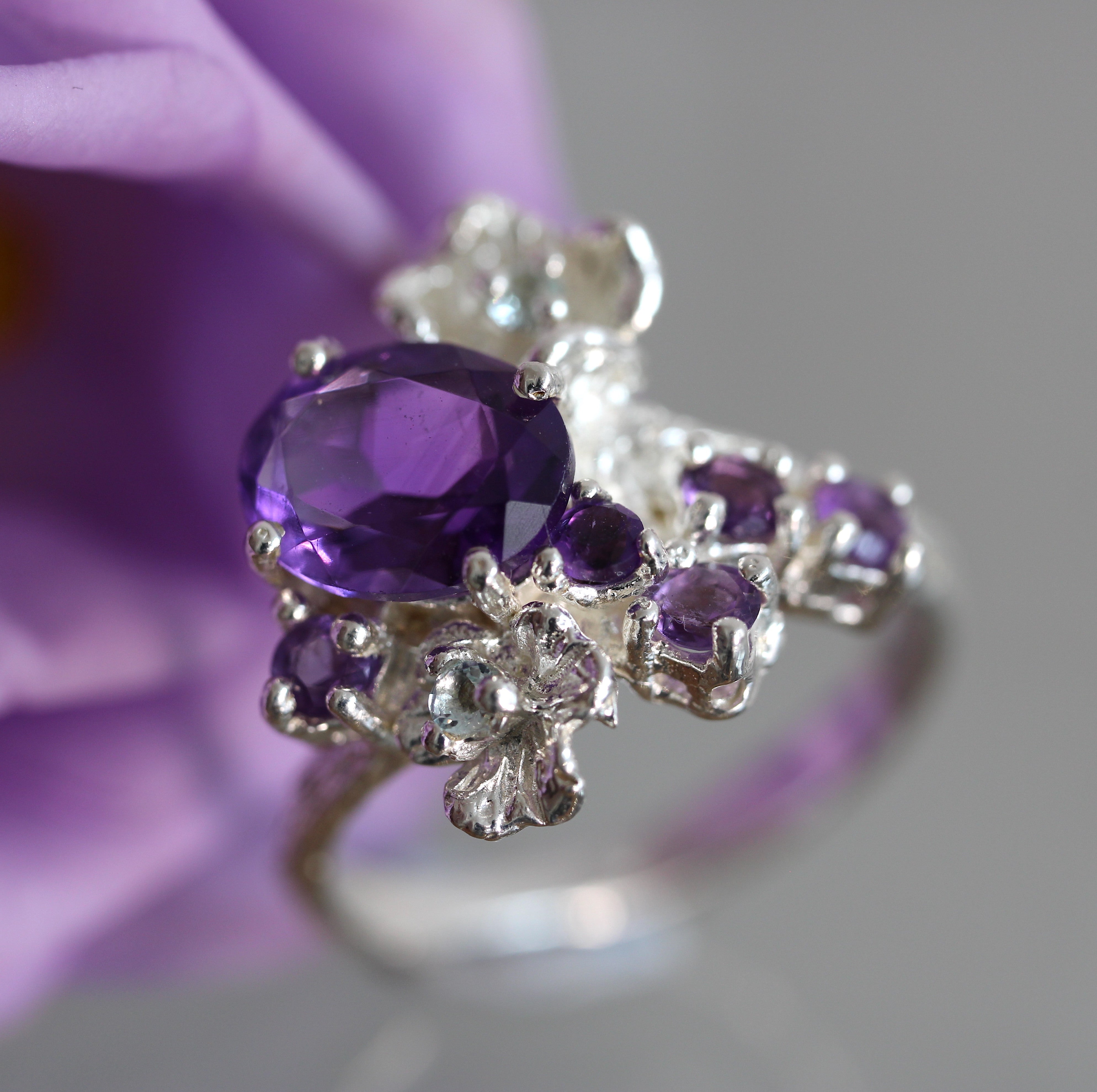 Silver ring with purple gemstones held against a purple flower background