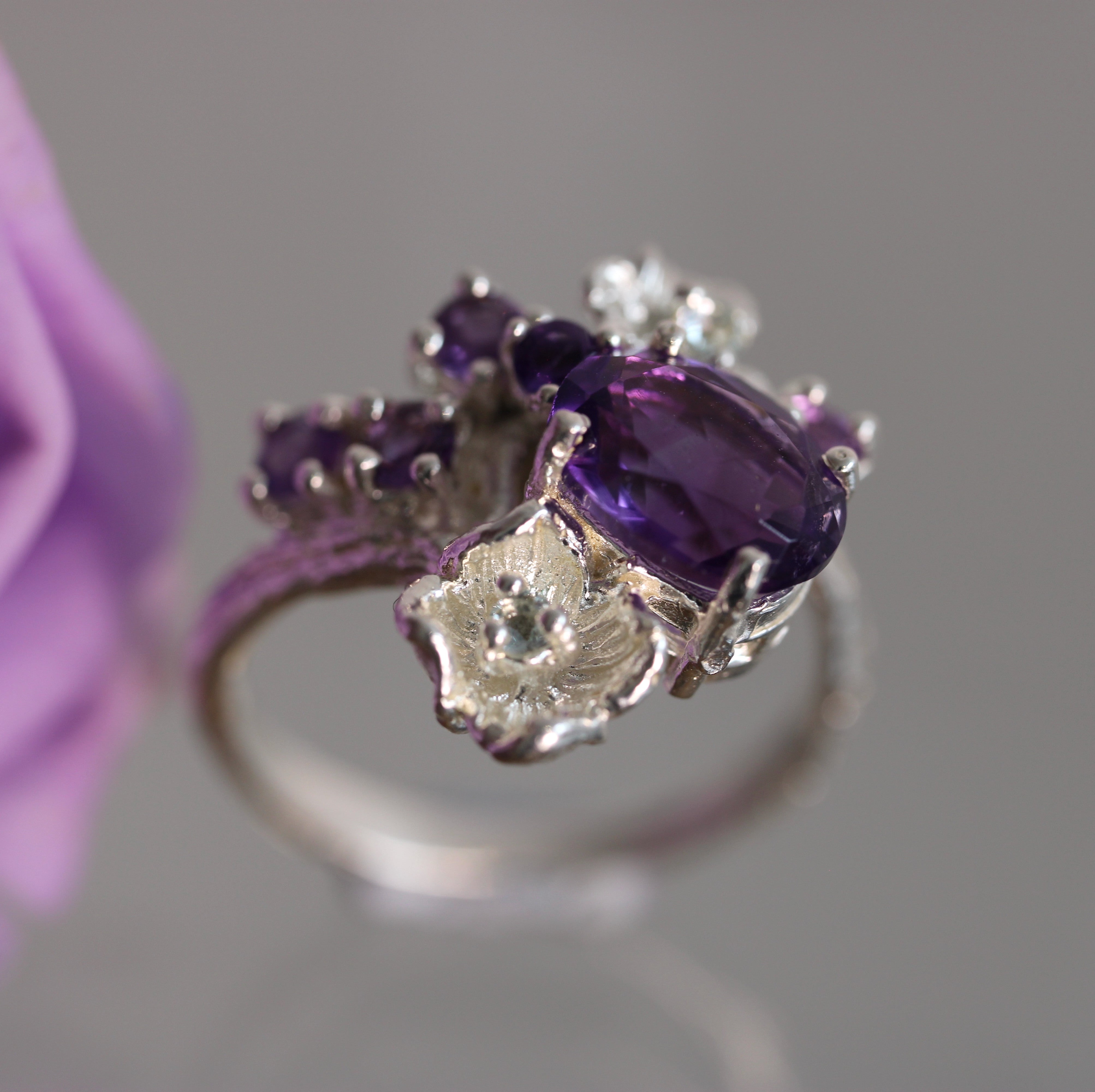 Silver ring with purple gemstones held against a gray background