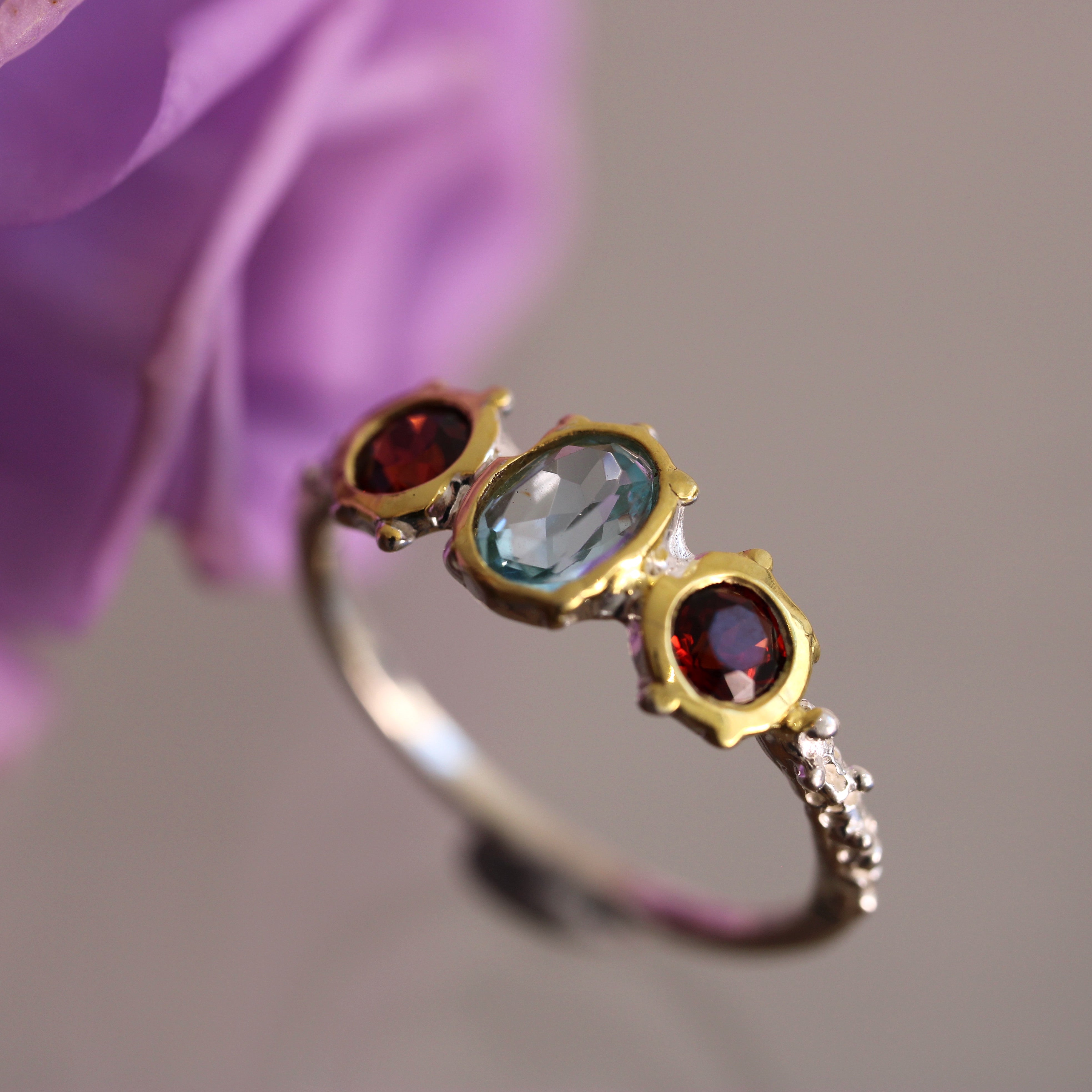 Ring with gemstones held against a blurred purple flower background