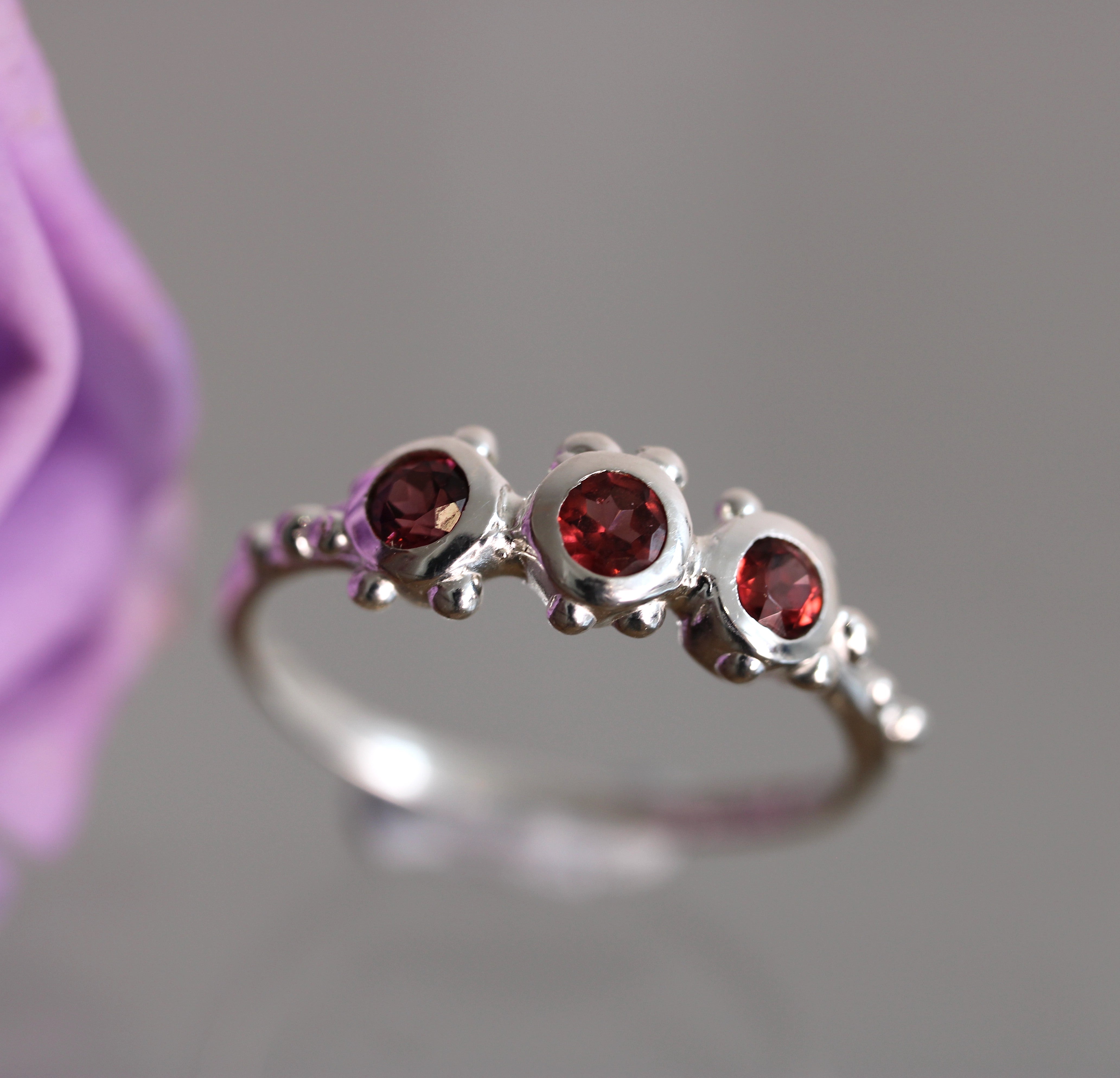 Silver ring with red gemstones against a blurred purple flower background