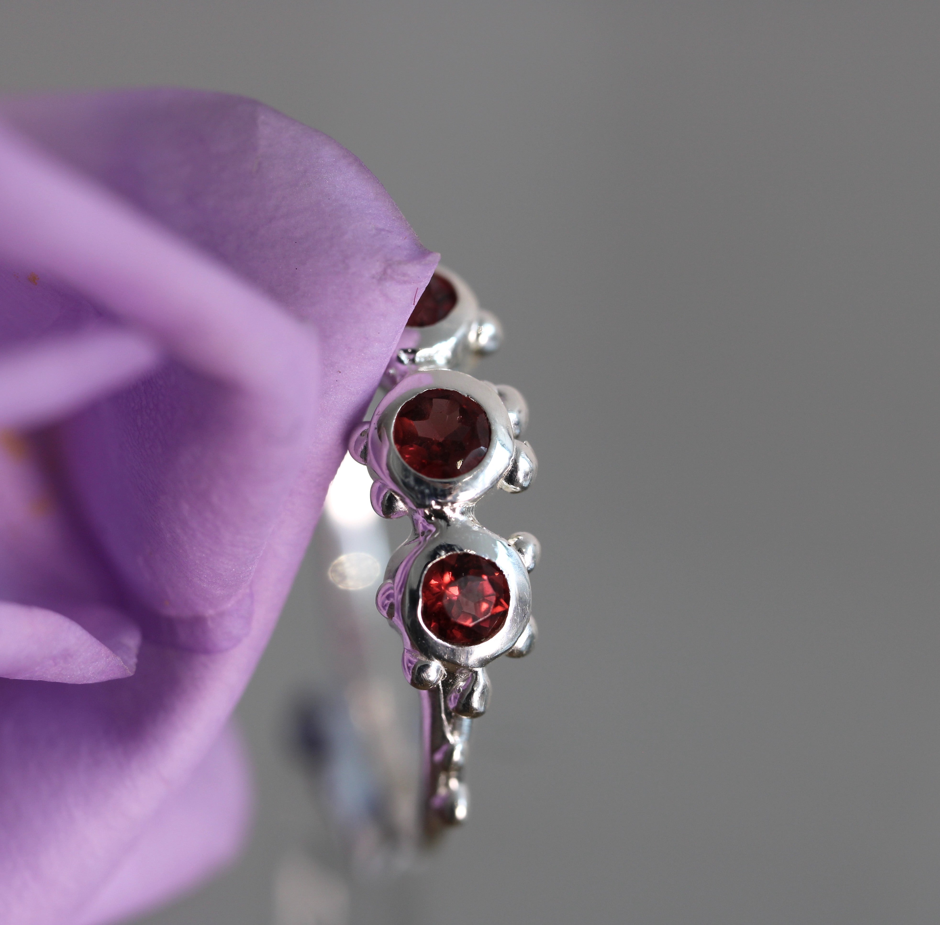 Silver ring with red gemstones held against a purple flower
