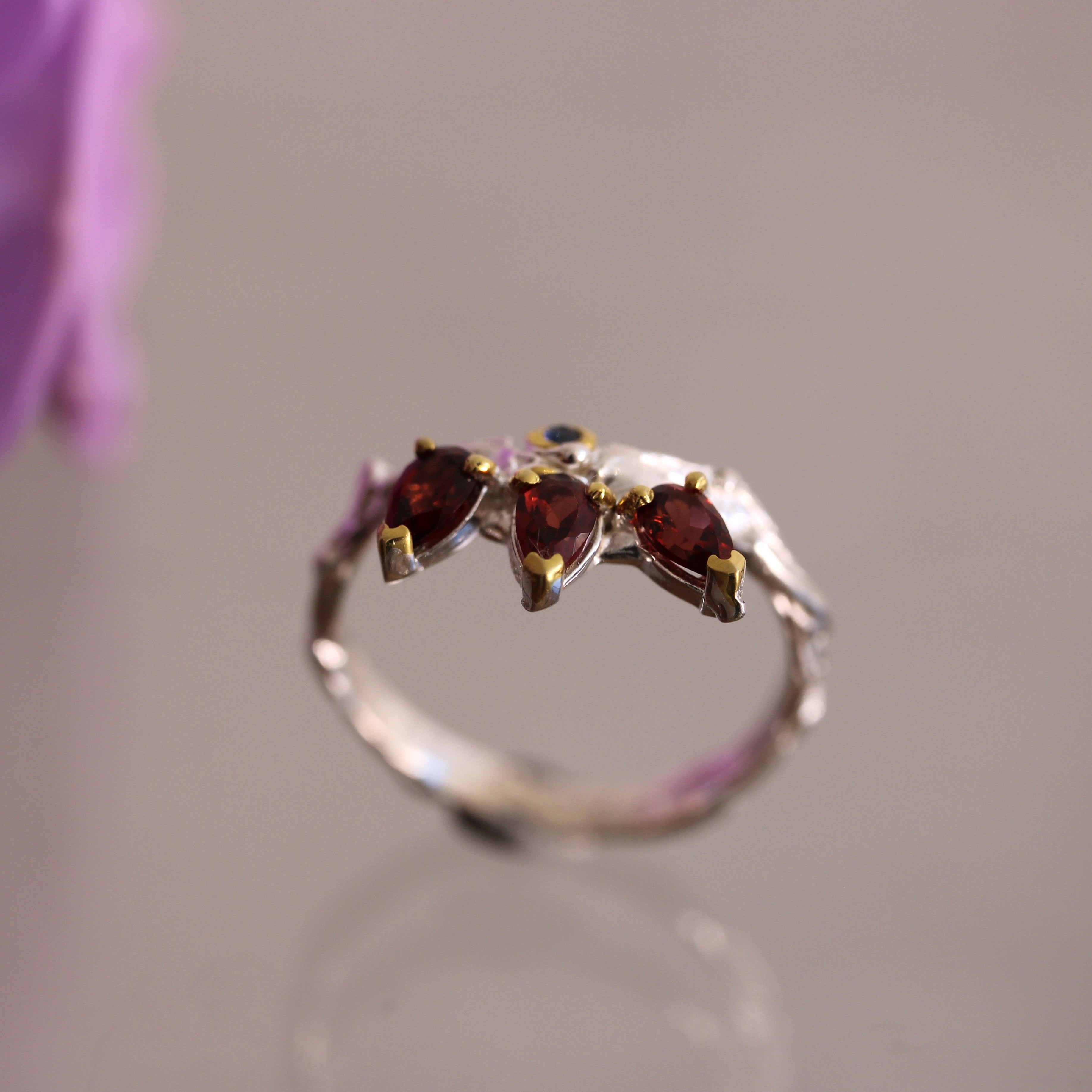 Silver ring with three red gemstones on a blurred background