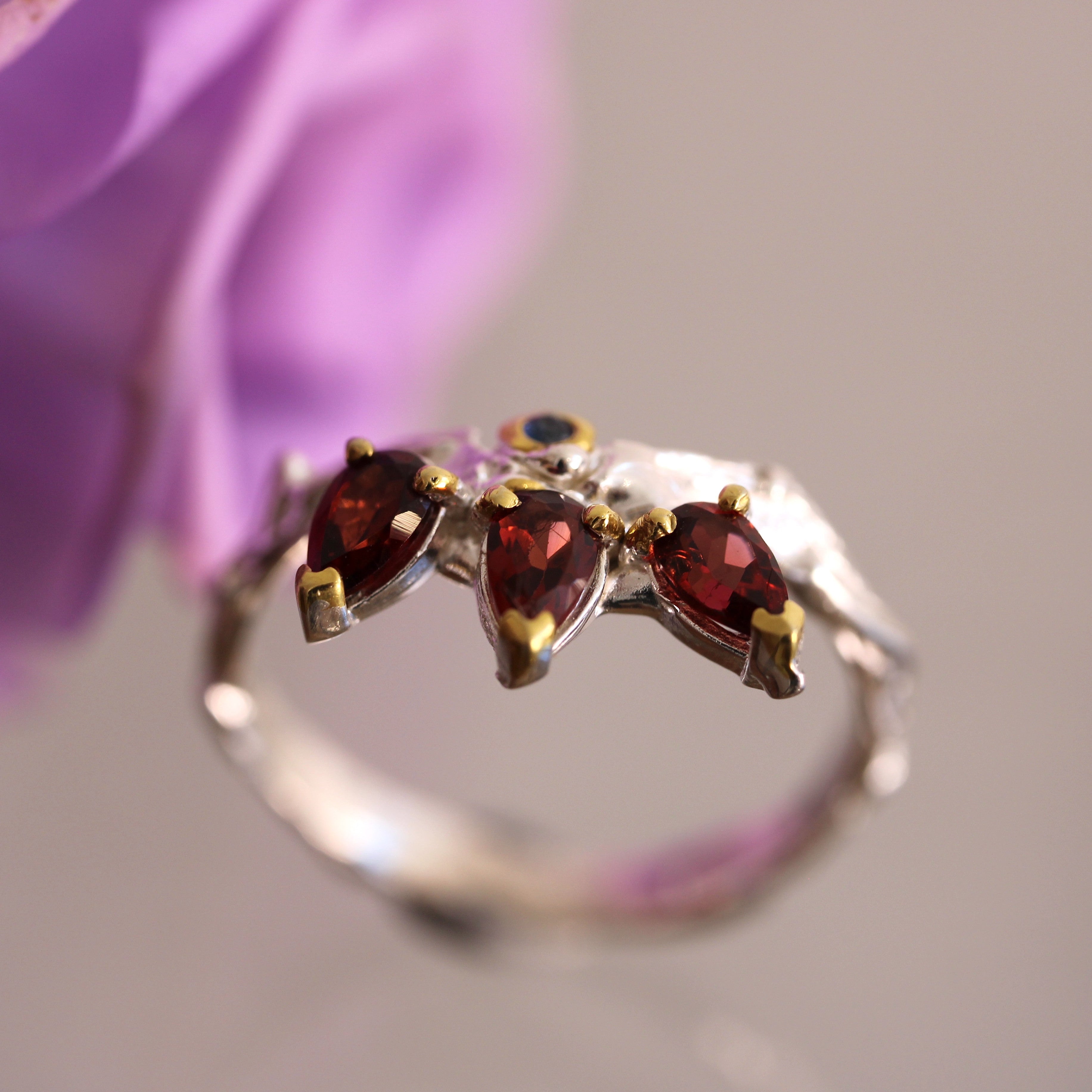 Silver ring with red gemstones against a blurred purple flower background