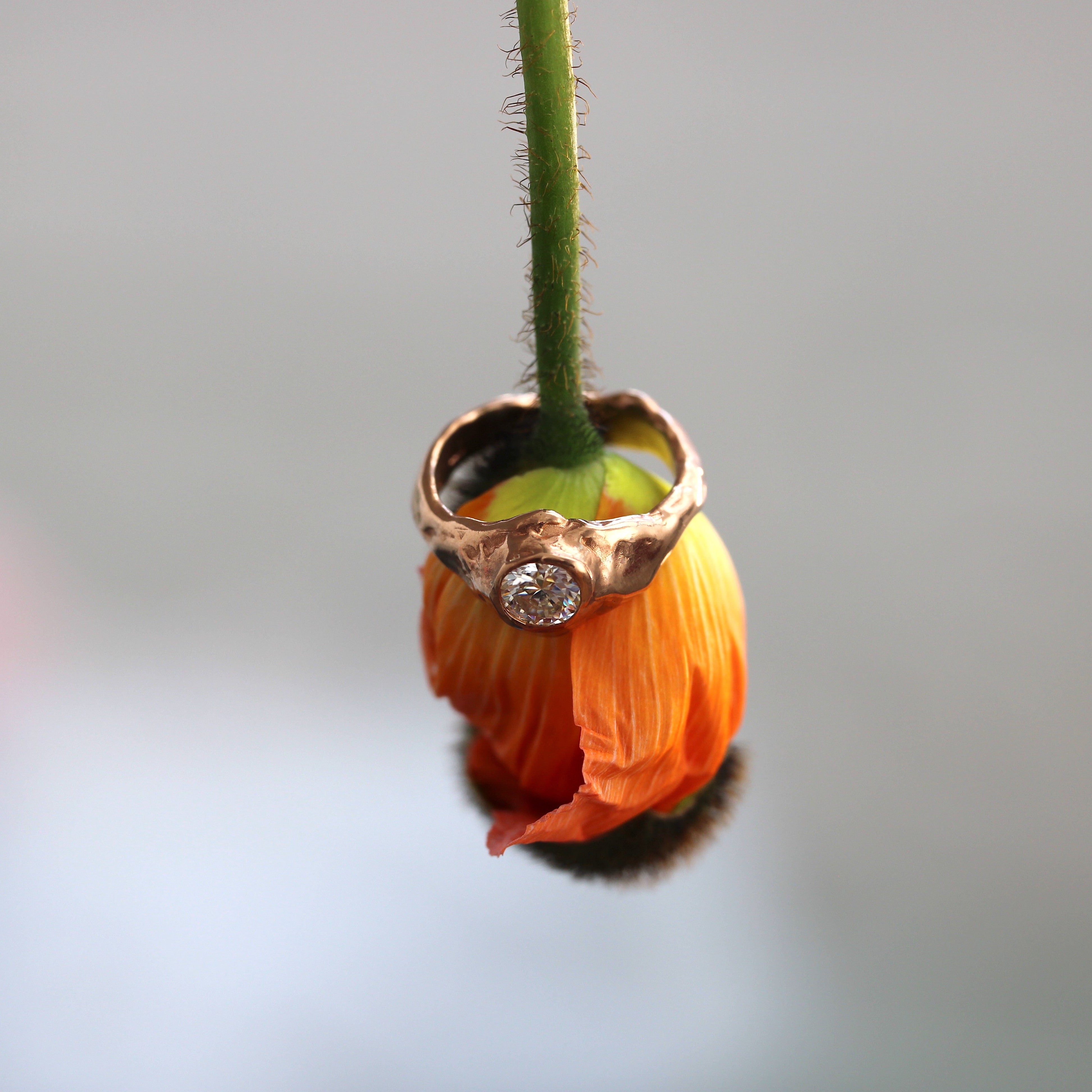 Gold ring with a diamond on an orange flower bud against a gray background