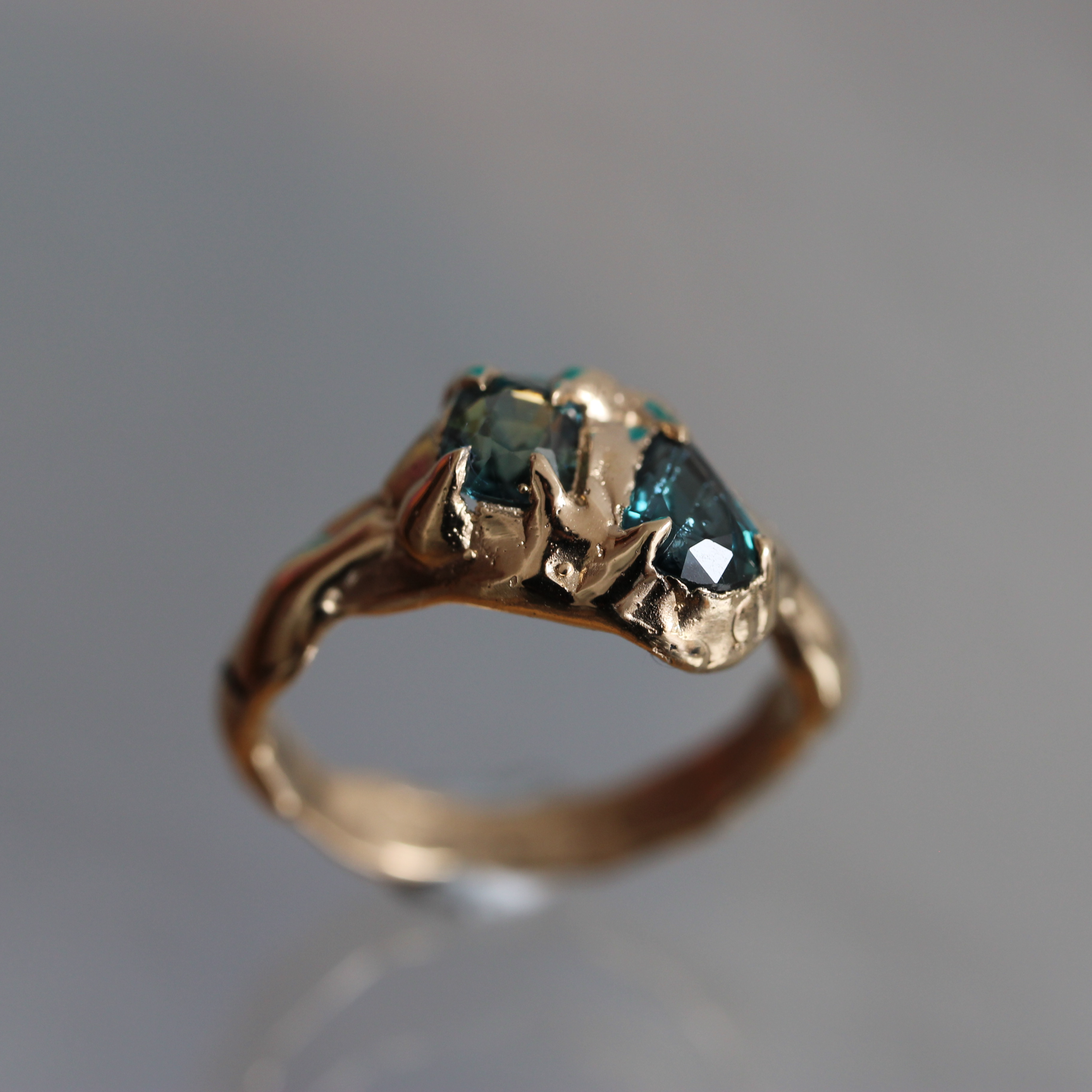 Gold ring with a green sapphire gemstone on a gray background