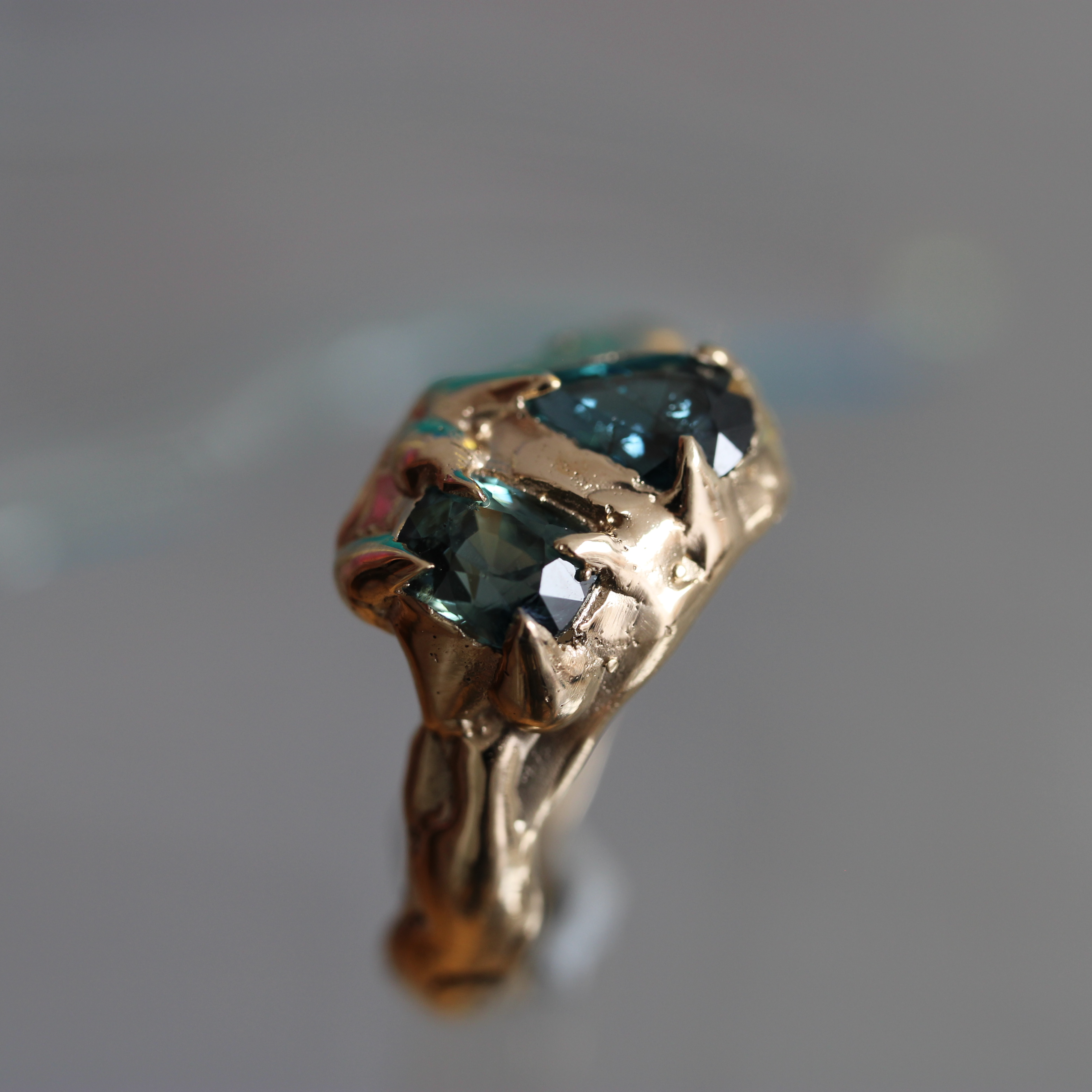 Gold ring with a blue green partii sapphire 
gemstone on a reflective surface