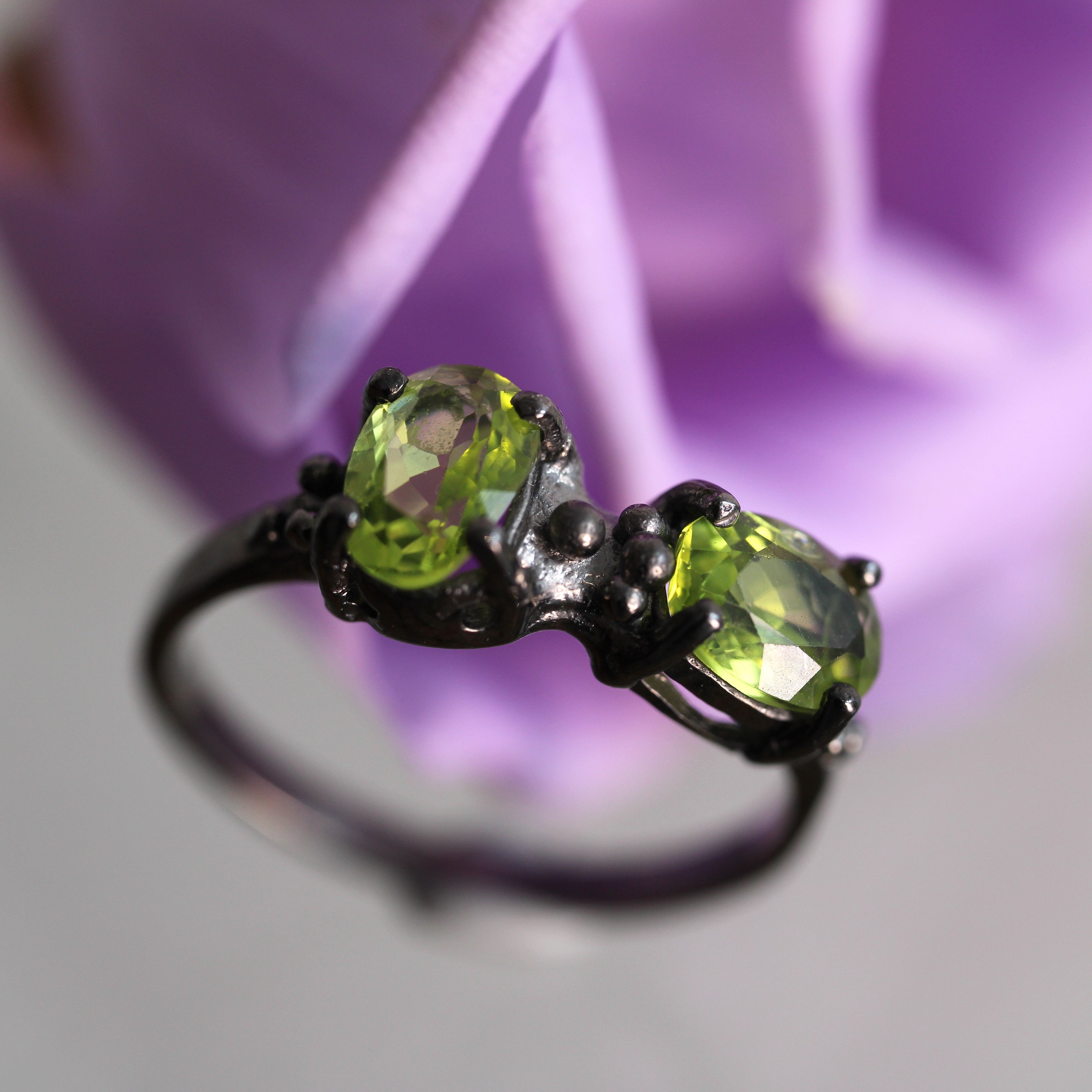 Ring with green gemstones on a blurred purple flower background