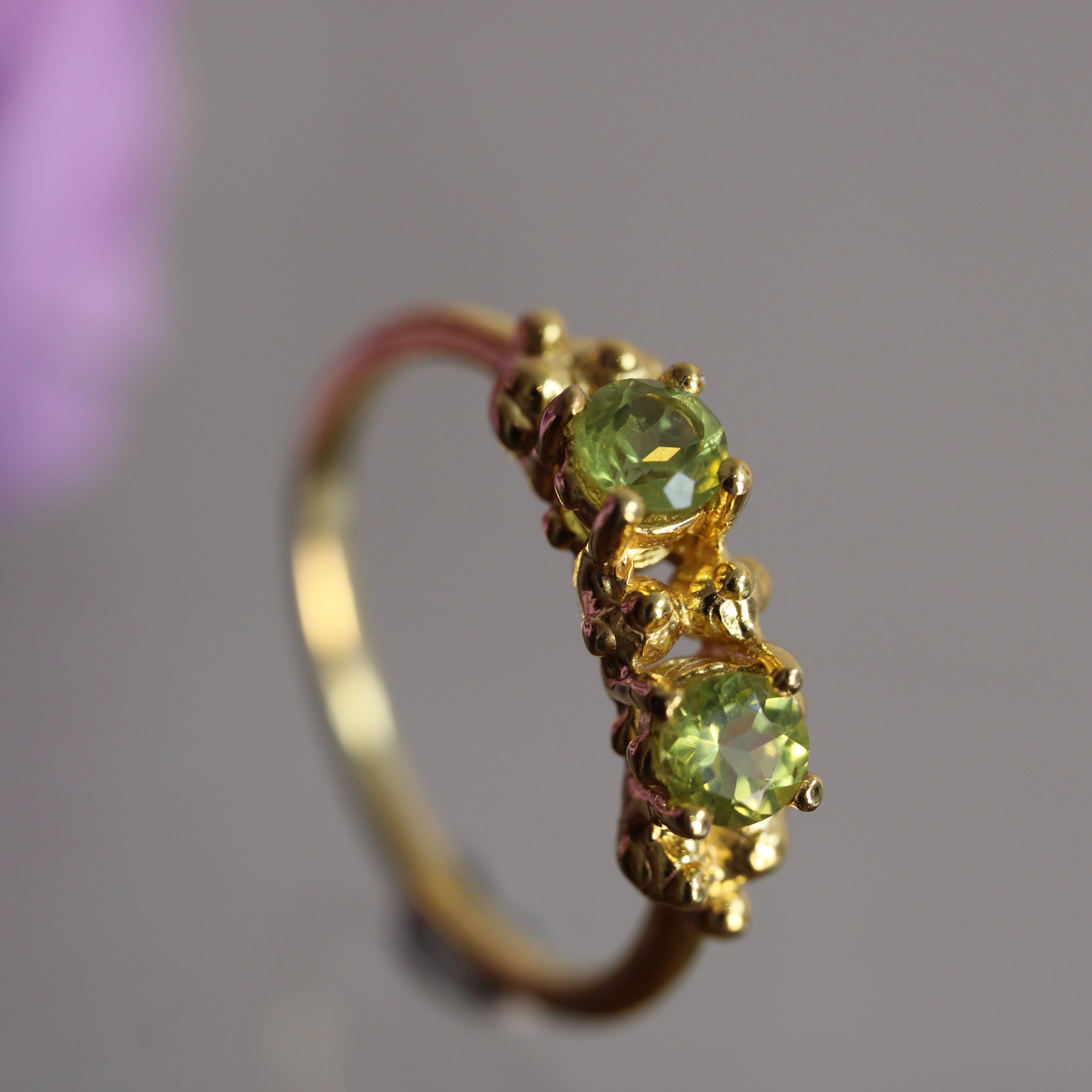 Gold ring with green gemstones on a blurred background